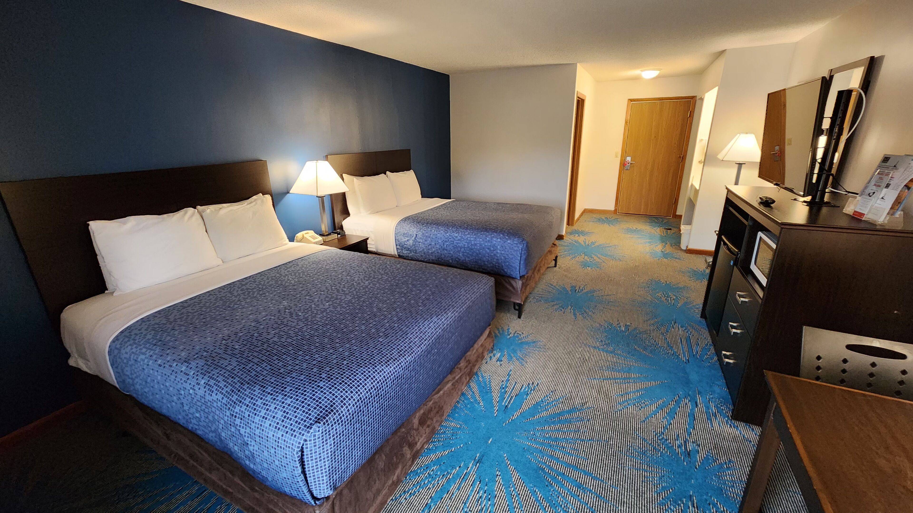 Habitación de hotel con dos camas, un escritorio, un espejo y una alfombra estampada.