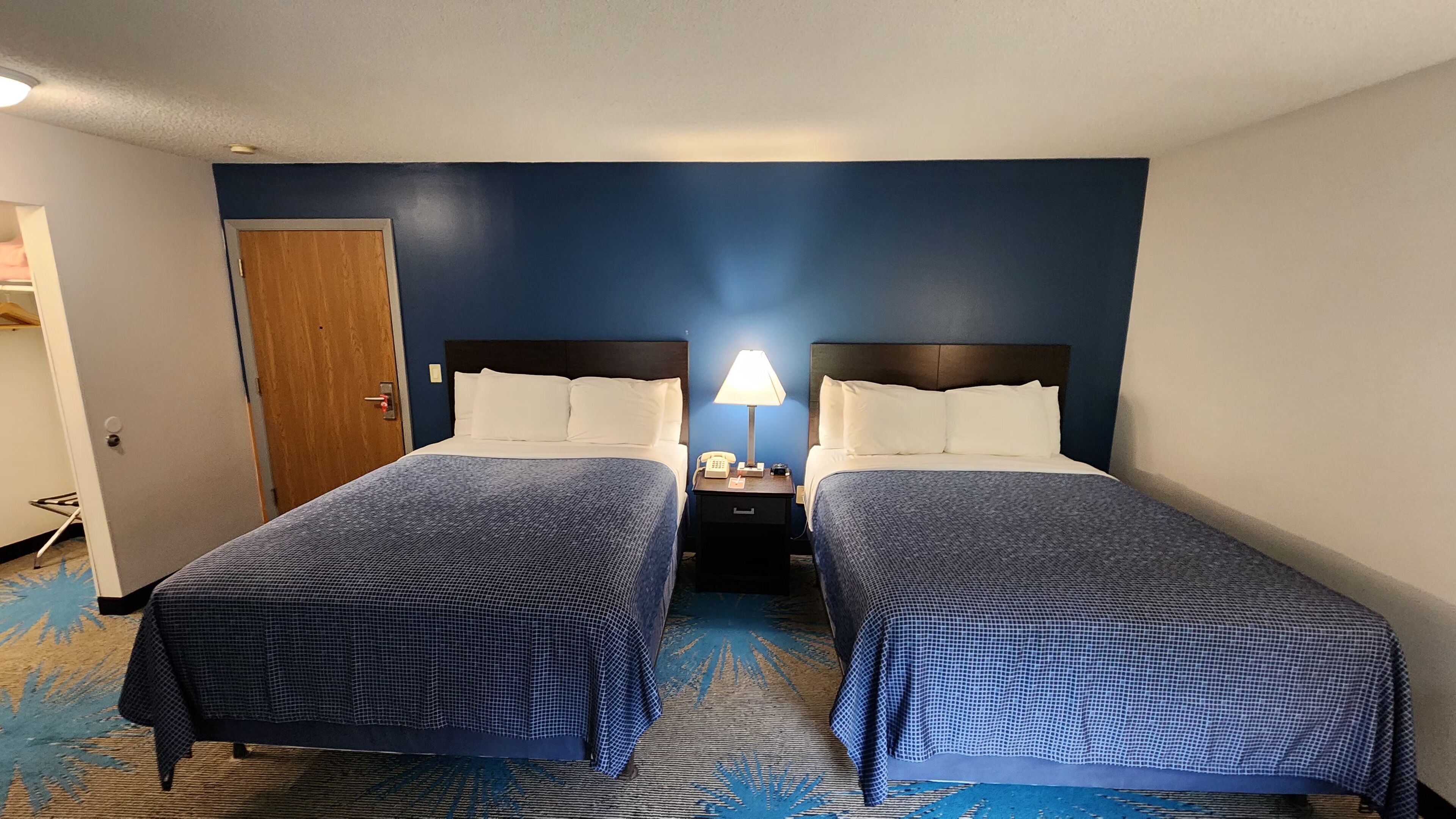 Une chambre d’hôtel avec deux lits, une table de chevet avec une lampe et une porte.