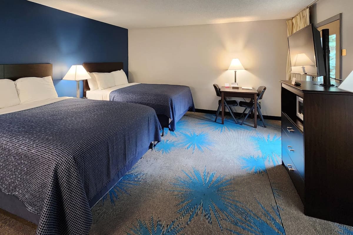 A hotel room with two beds, a desk, a chair, a TV, and a dresser.