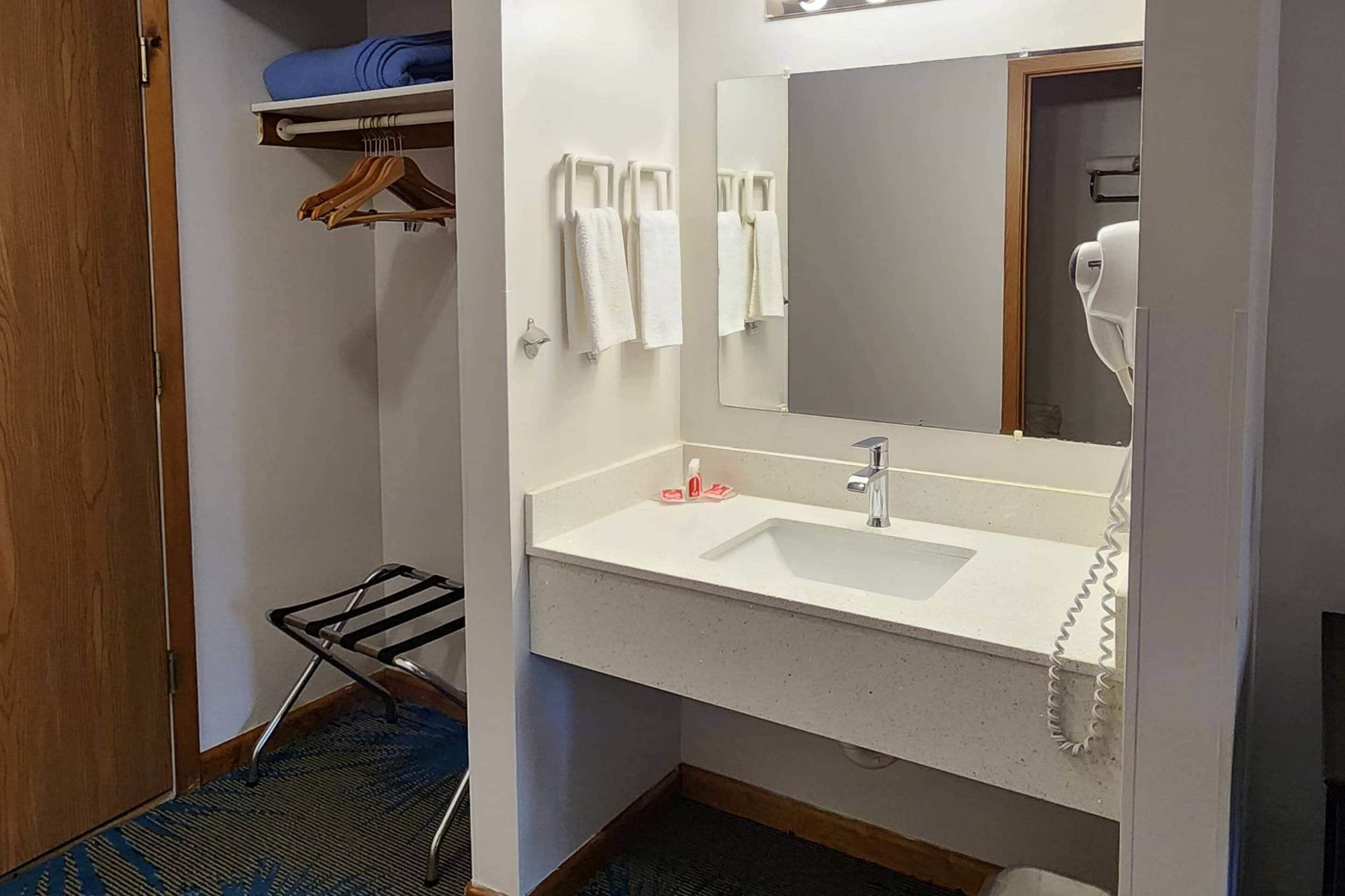 Un baño de hotel con un lavamanos blanco, un espejo, un perchero para toallas y un secador de pelo.