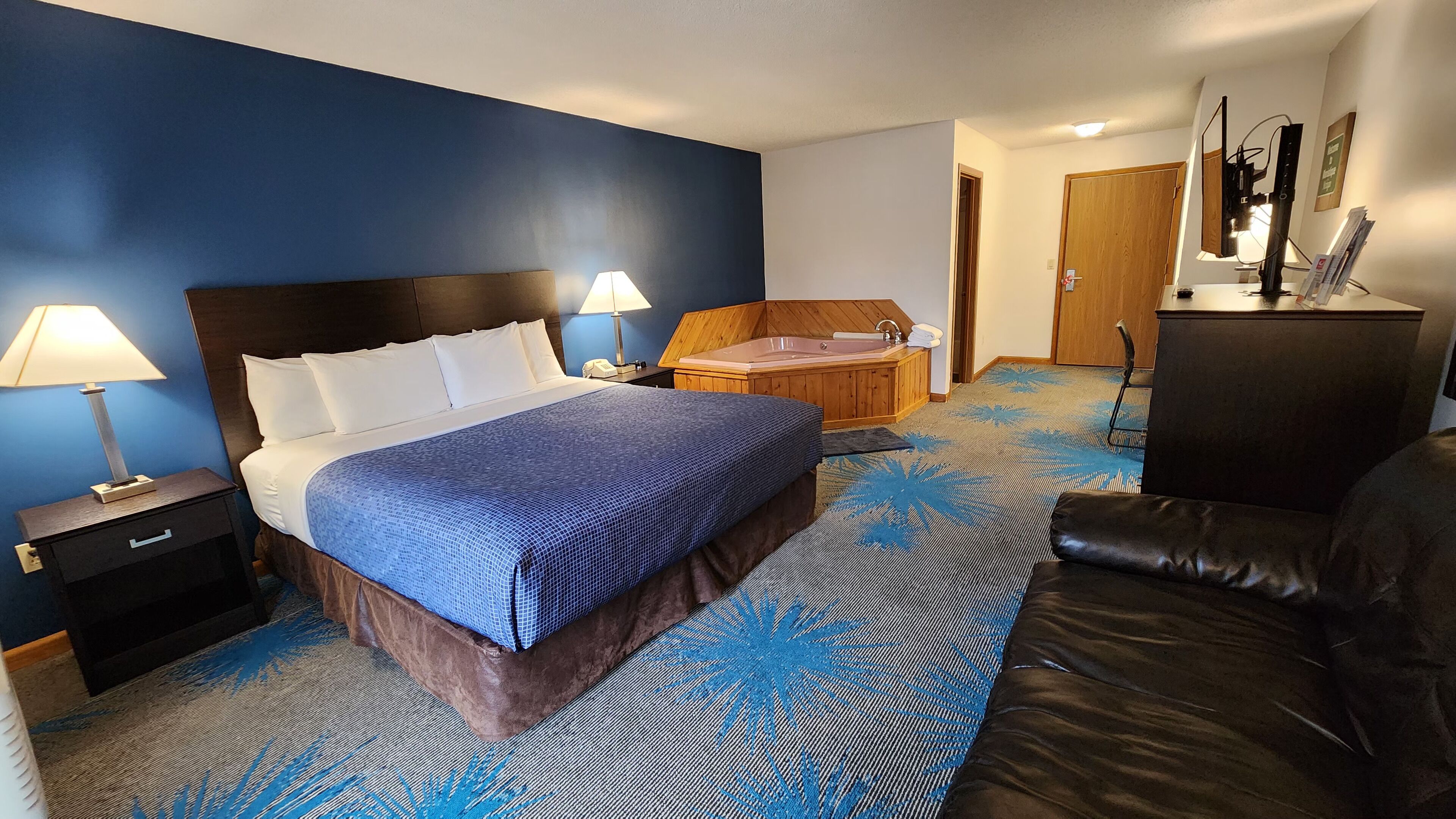 Une chambre d’hôtel avec un lit, un bureau, une chaise, une baignoire et une lampe de bureau.