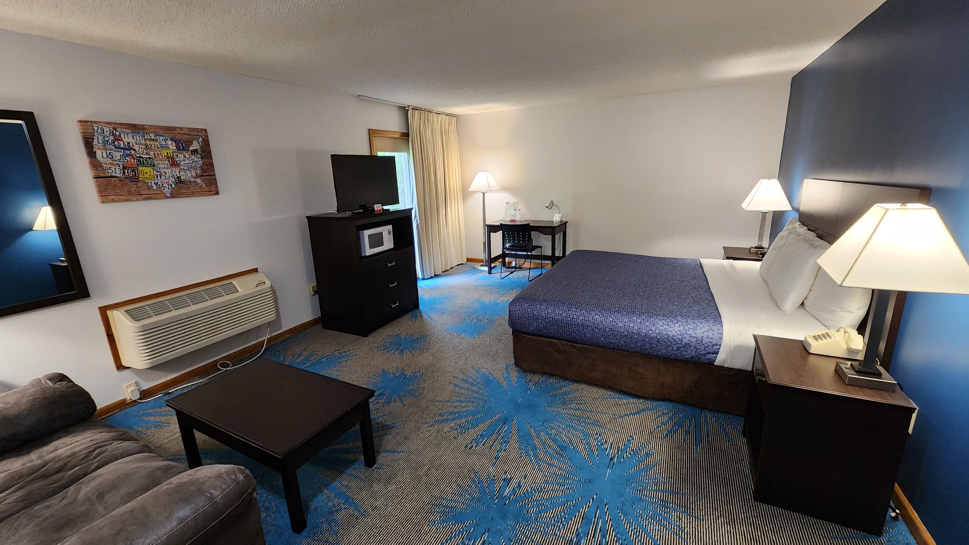 A hotel room with a bed, a desk, a chair, a TV, a microwave, a heater, and a couch.