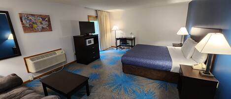 A hotel room with a bed, a desk, a chair, a TV, a microwave, a heater, and a couch.