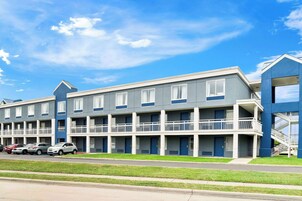 Un motel de varios pisos con balcones, un estacionamiento y cielo despejado.