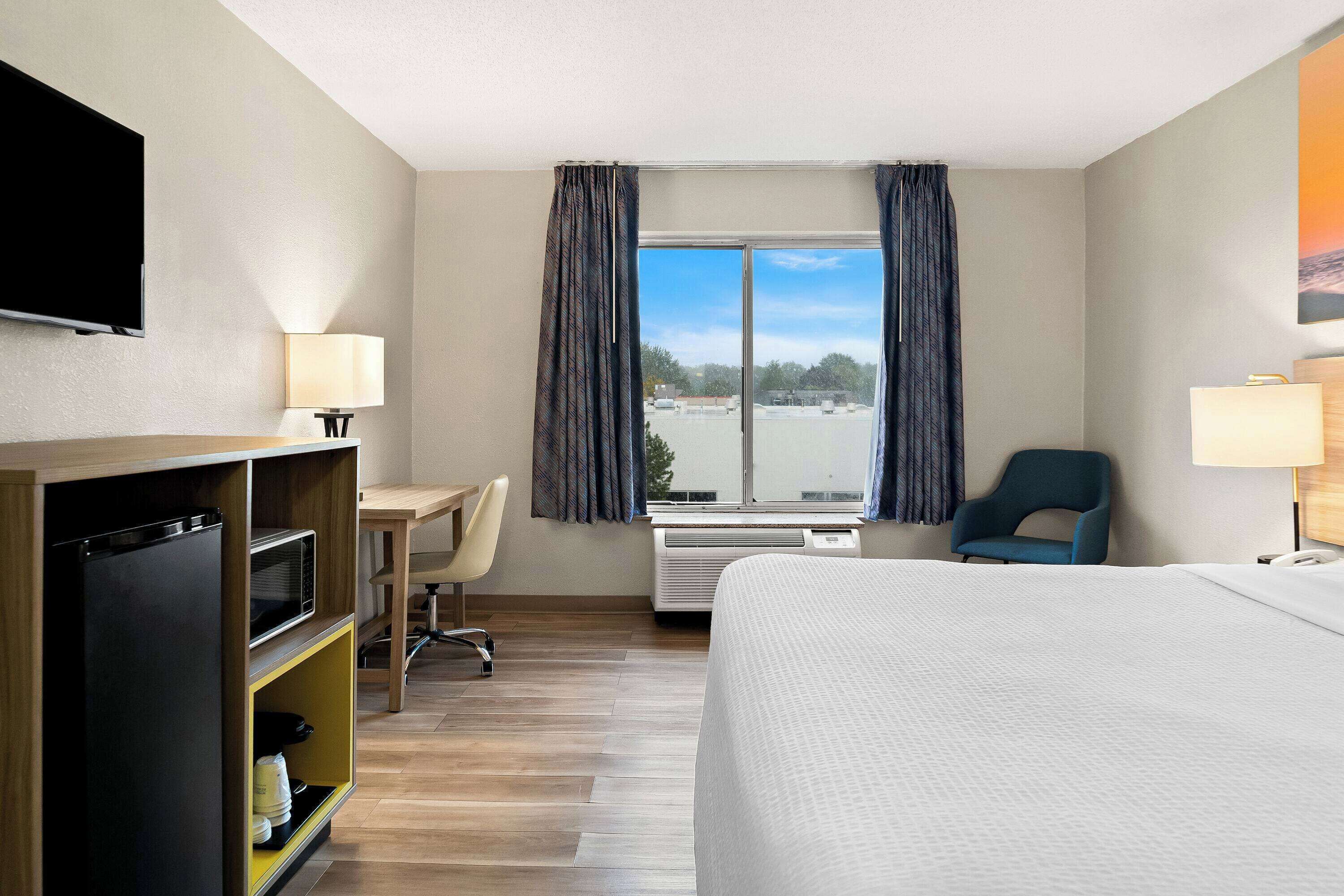 Habitación de hotel con cama, escritorio con silla, televisión, aire acondicionado y ventana con cortinas.