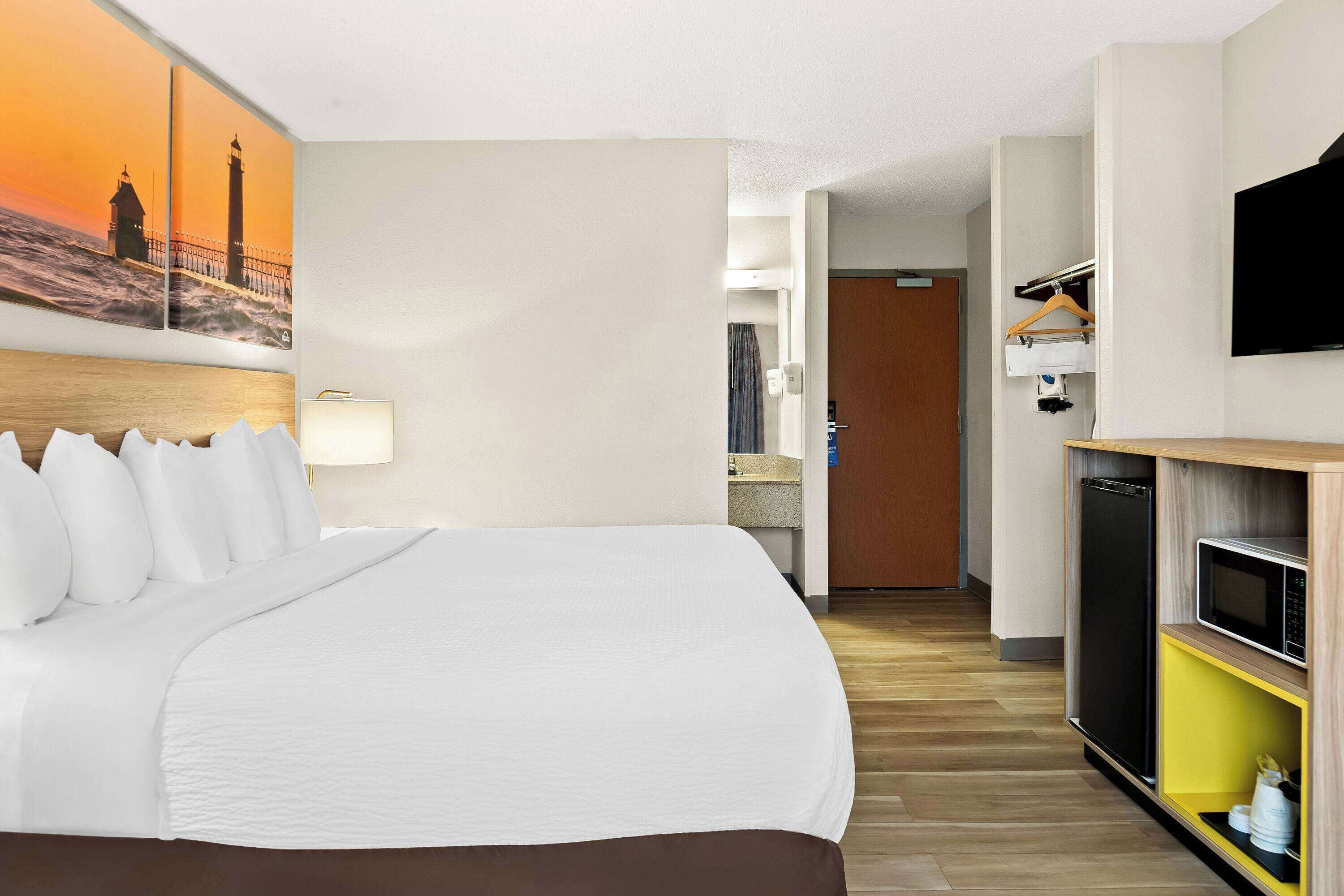 Habitació d'hotel amb un llit gran, un quadre d'un far, una televisió i una cuineta.