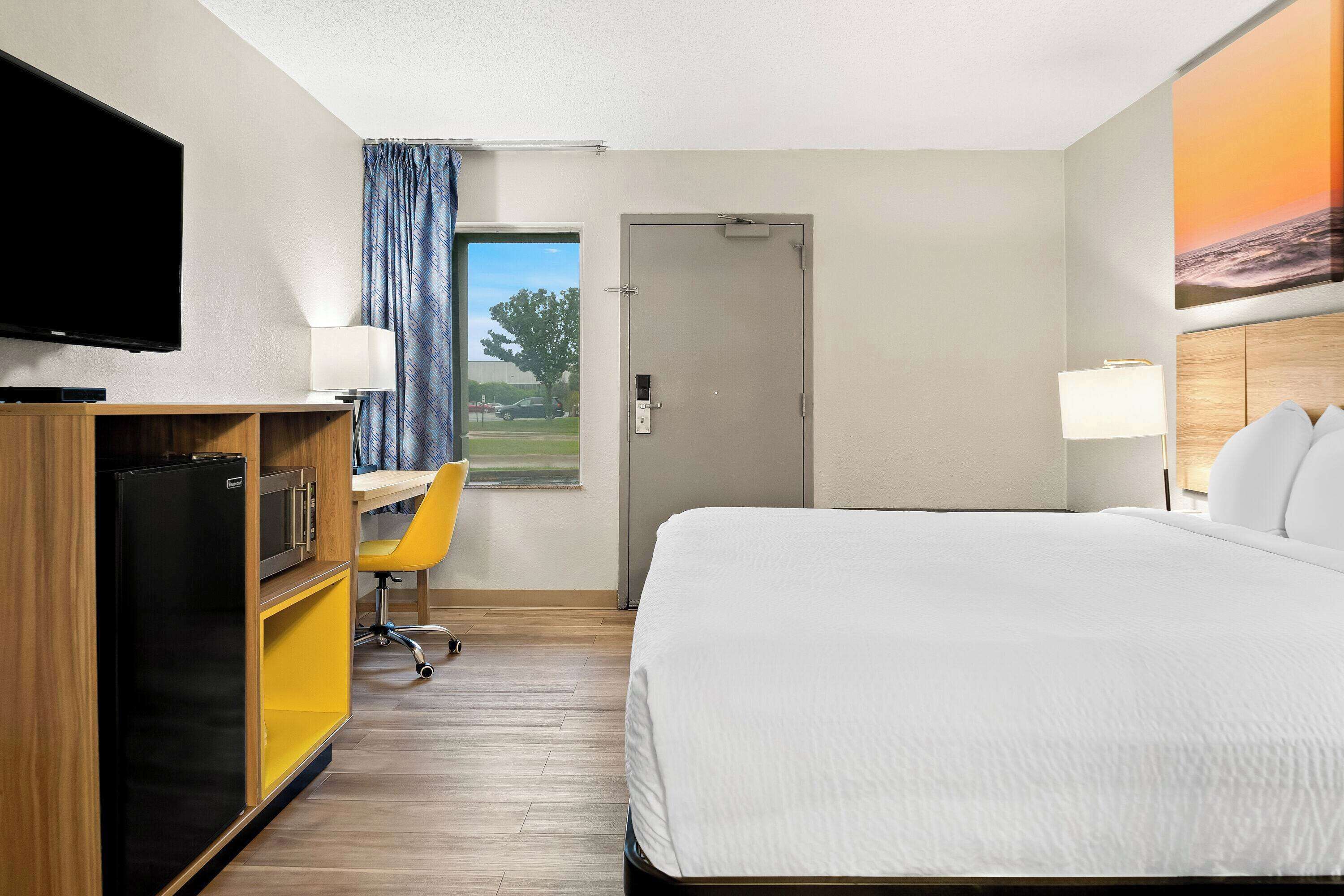 Una habitación de hotel con una cama, un escritorio con una silla, un televisor y una puerta.