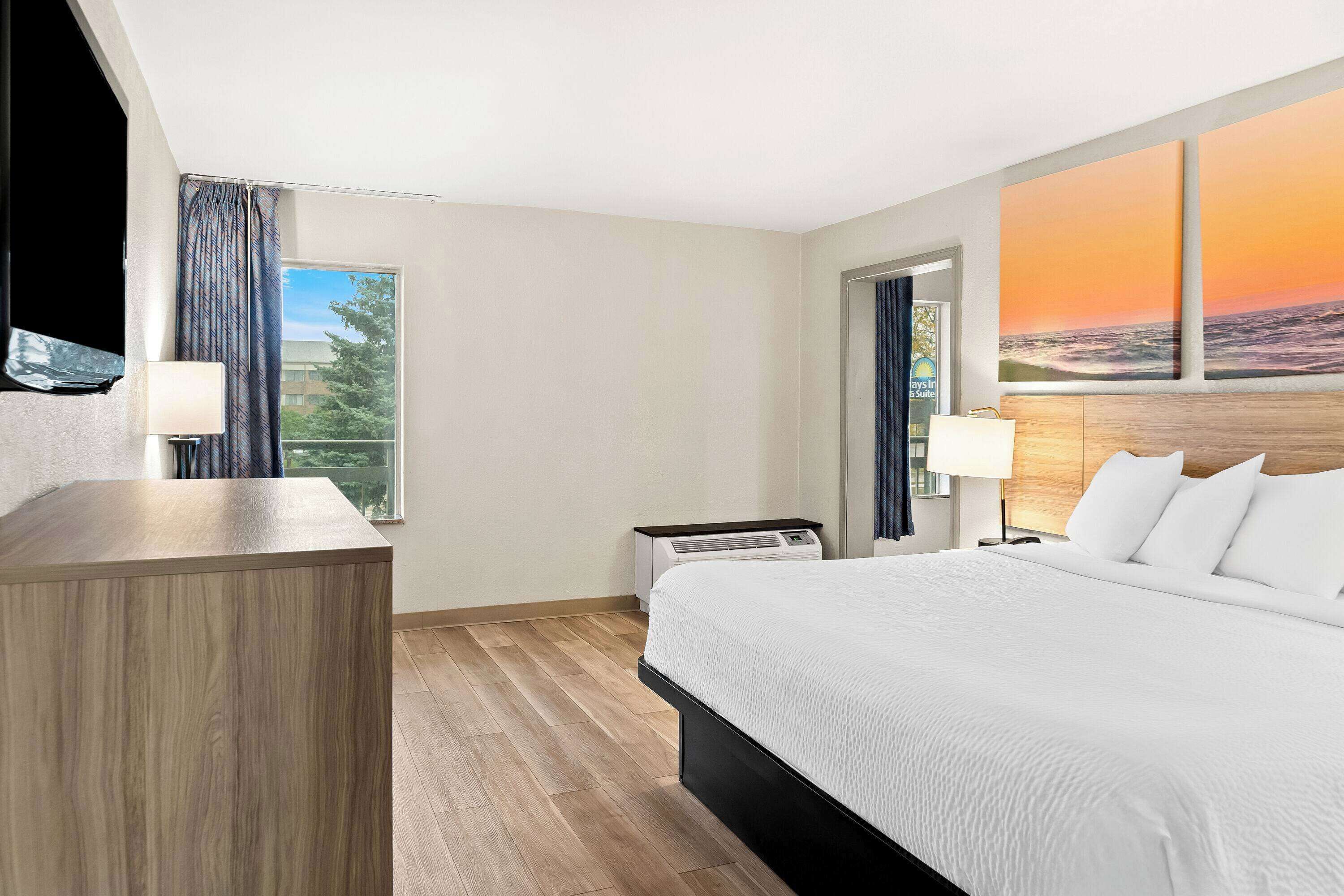 A hotel room with a bed, a desk, a TV, and a large window with a view.