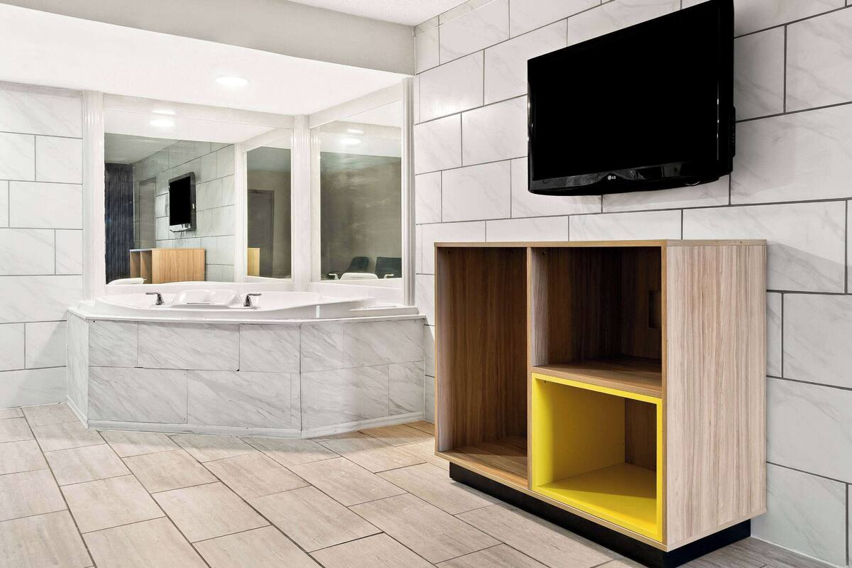 A modern bathroom with a large mirror, a bathtub, a vanity with two sinks, and a mounted television.
