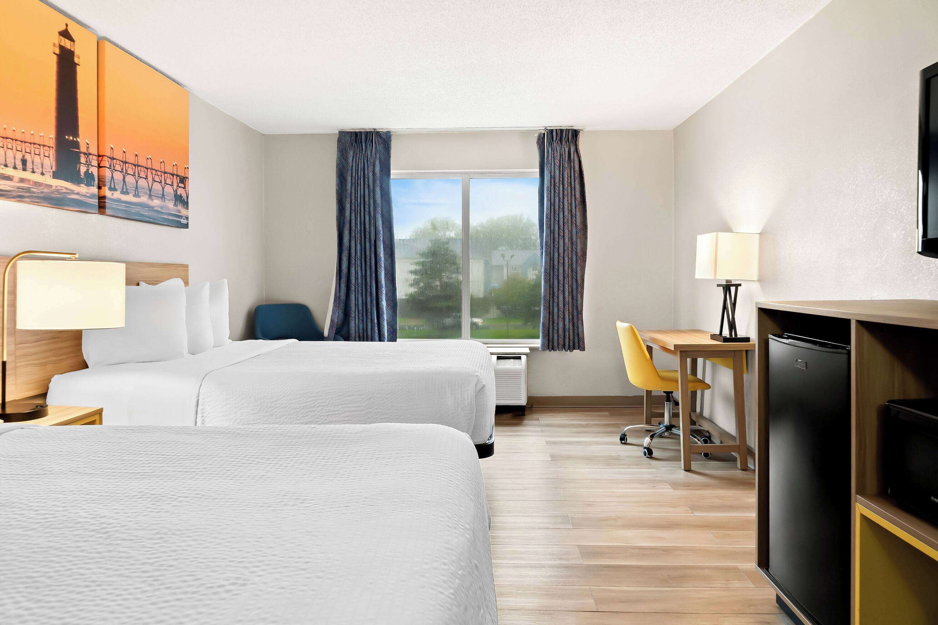 A hotel room with two beds, a desk, a chair, a TV, and a window with curtains.