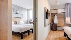 Una habitación de hotel moderna con dos camas, suelo de madera, una litera y un escritorio.