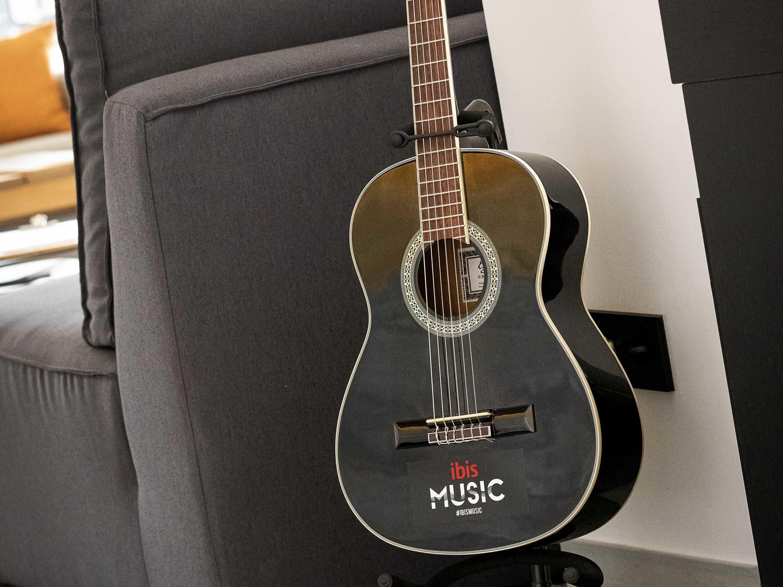 Una guitarra con la marca 'ibis MUSIC', colgada de una silla tapizada de gris.