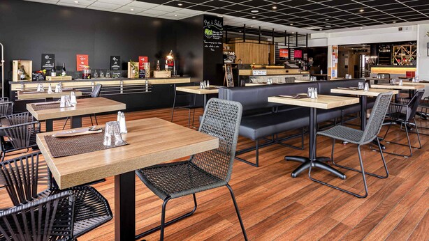 Un interior de restaurante moderno con mesas de madera, sillas de malla negra y un diseño de techo en blanco y negro.