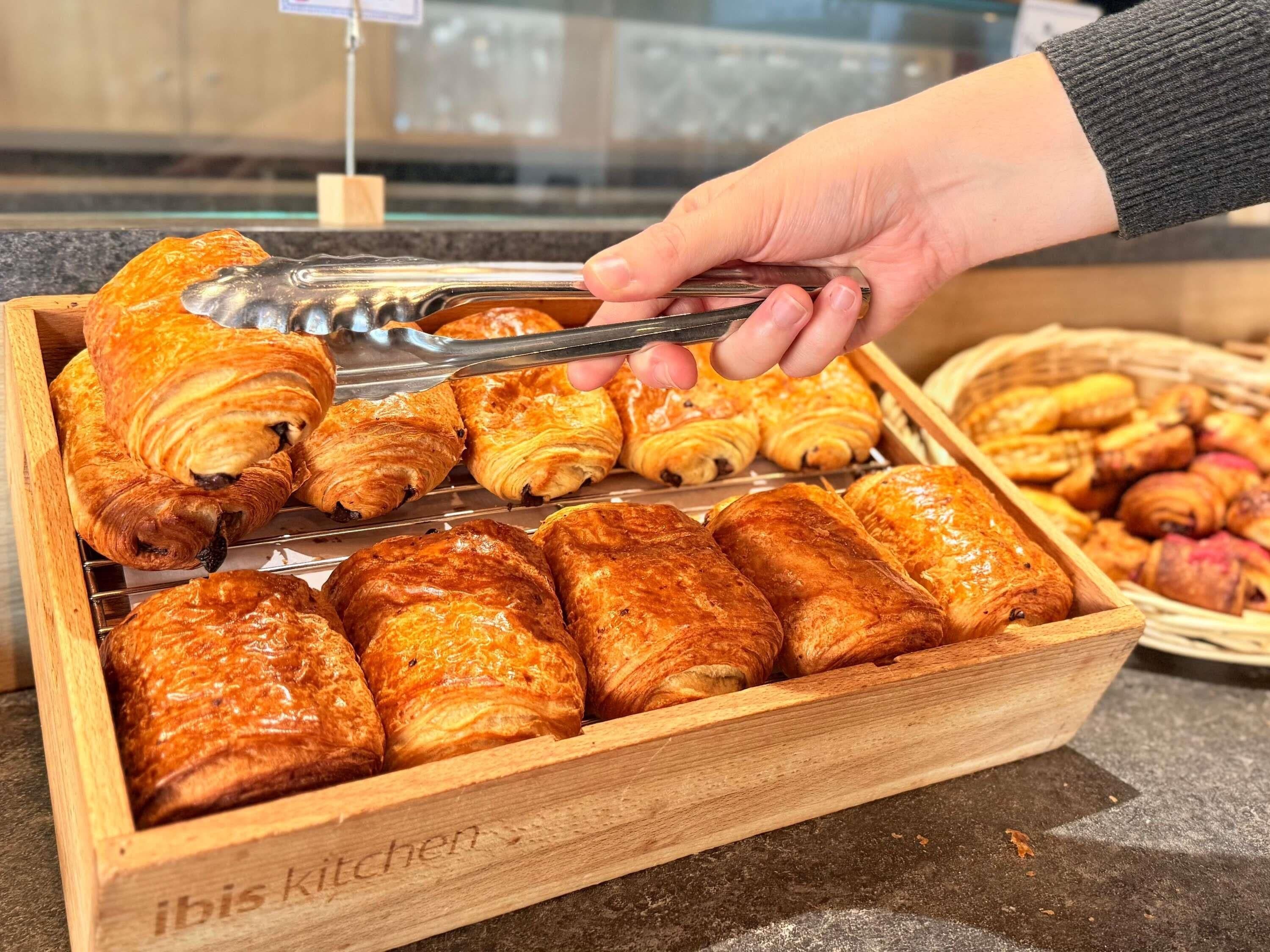 Una caja de madera llena de pasteles variados, incluyendo croissants y otras delicias horneadas, exhibida en una panadería.