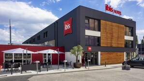Un hotel moderno con un llamativo letrero de 'ibis', mesas al aire libre y un área de estacionamiento.