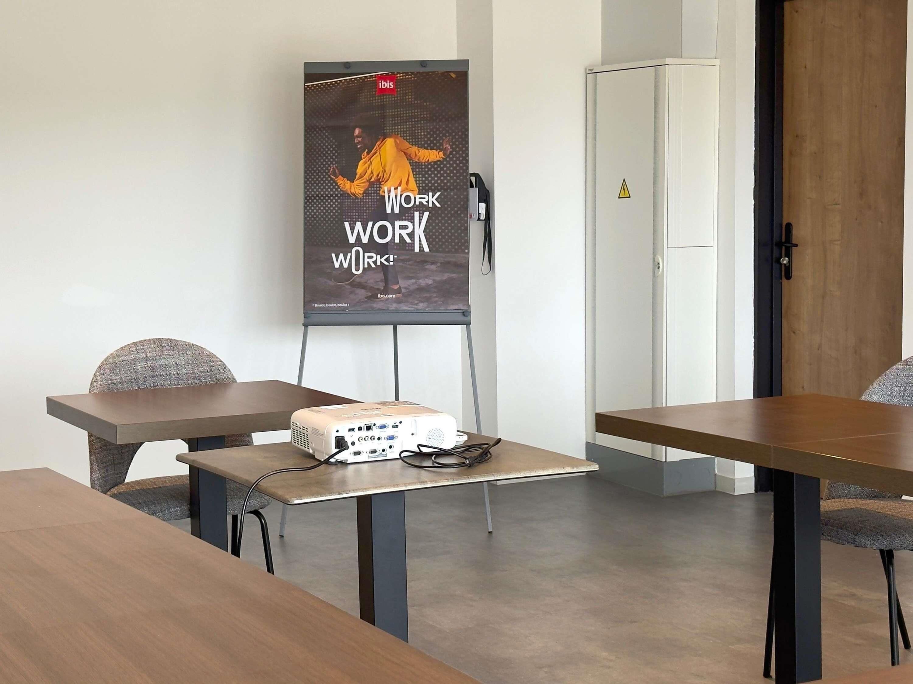 Une salle de conférence équipée d’un projecteur, avec une affiche accrochée au mur et une porte.