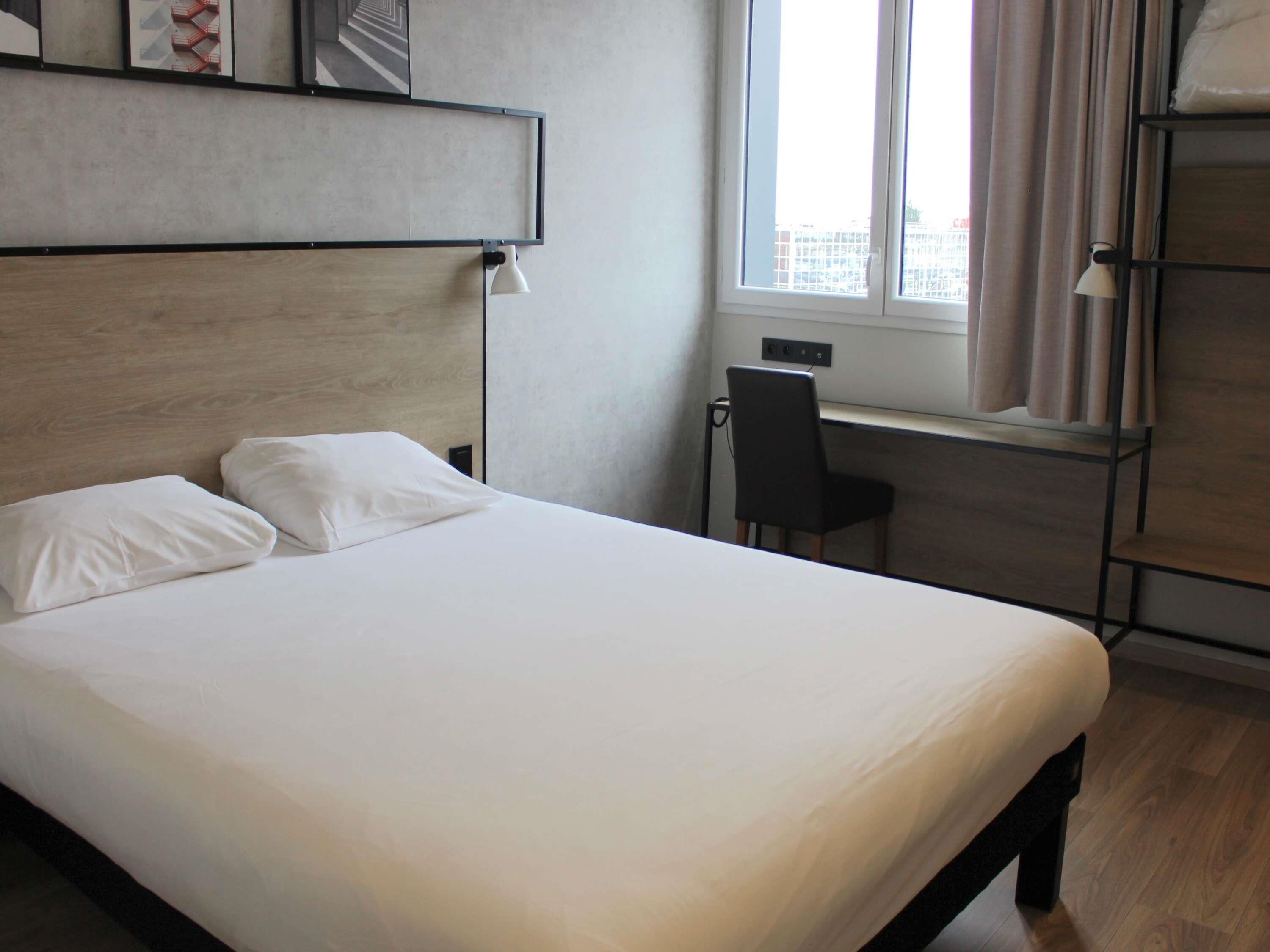 Een hotelkamer met een bed, een bureau, een stoel en een raam met gordijnen.
