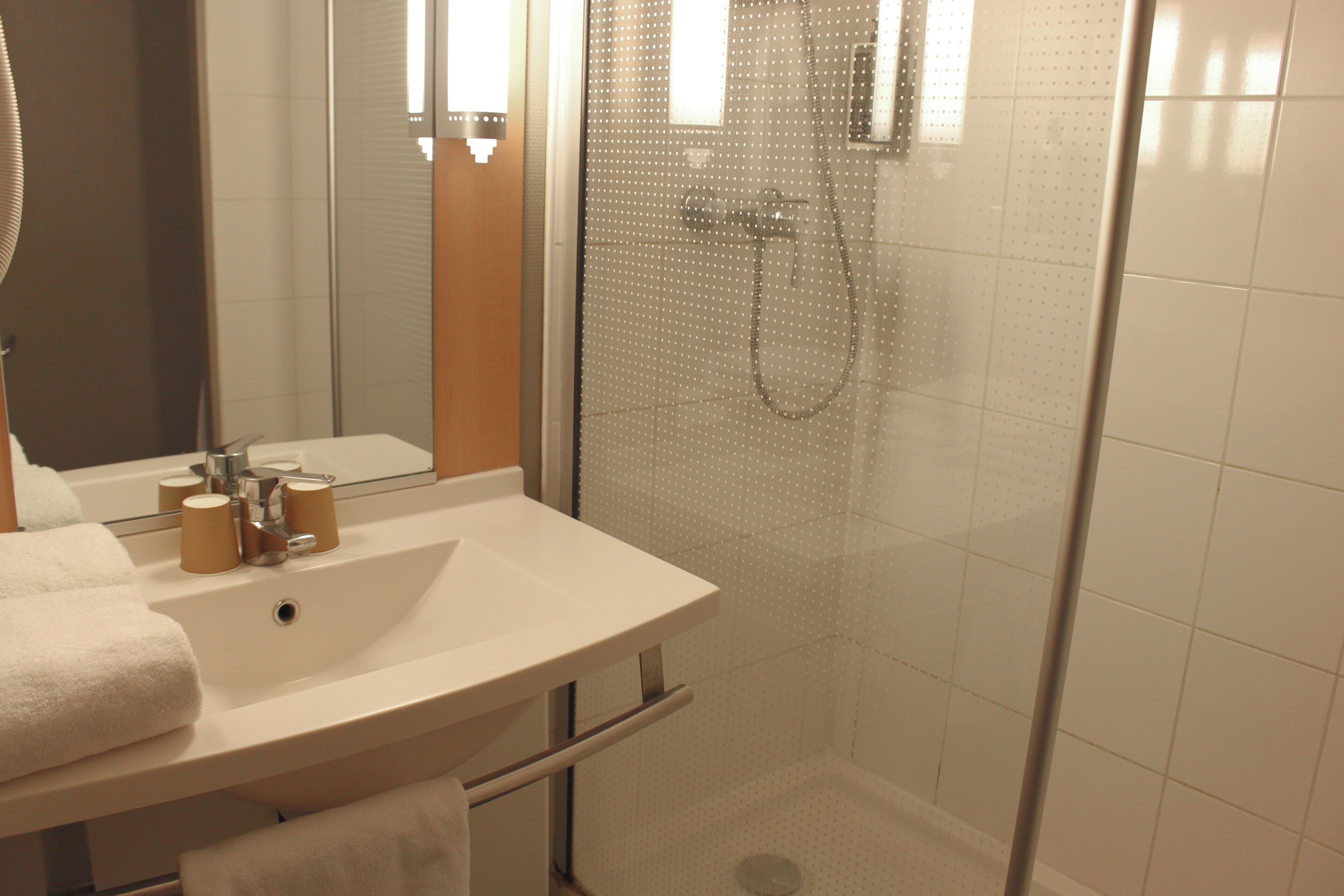 Un baño con lavamanos blanco, espejo y ducha.