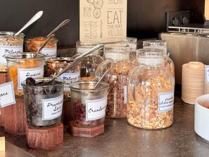 Variedad de alimentos en frascos con etiquetas, un letrero que dice '¡COME A TU GUSTO!' y pilas de platos.