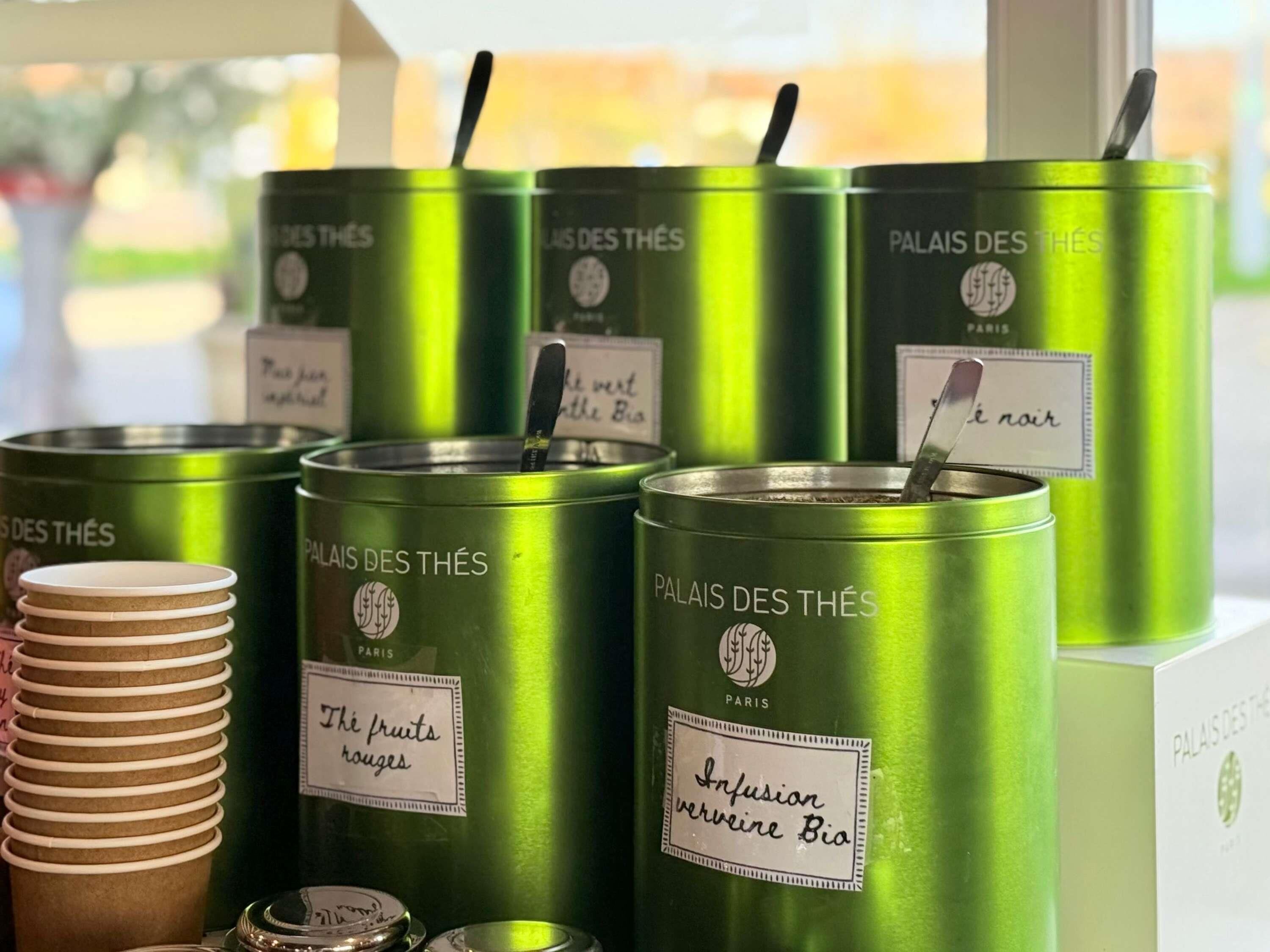 Meerdere groene metalen containers met de aanduiding 'Palais des Thés', elk met verschillende teksten die diverse theesmaken beschrijven.