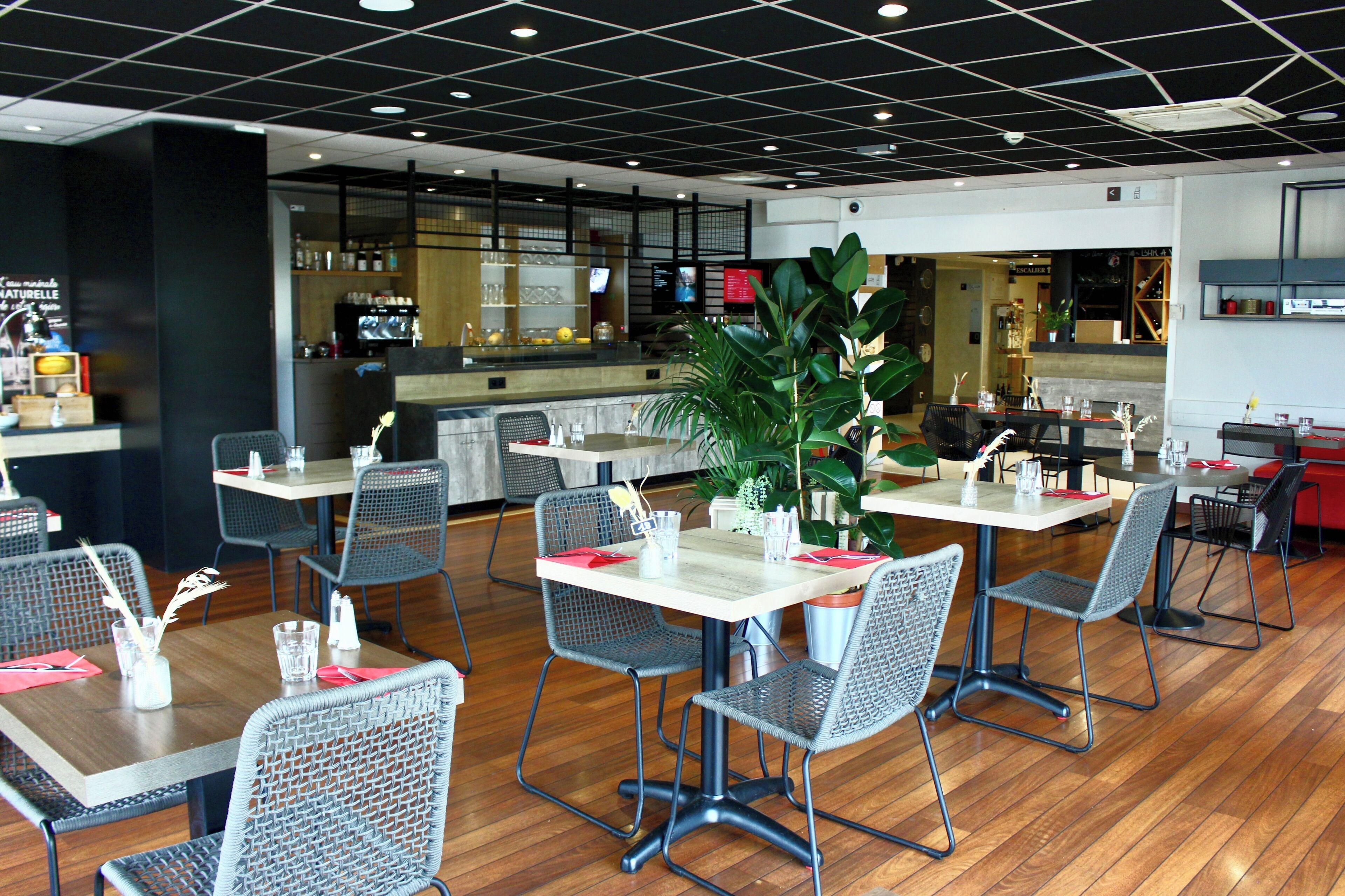 Un restaurante moderno con un diseño limpio y abierto, que cuenta con varias mesas y sillas, una planta central y una zona de barra al fondo.