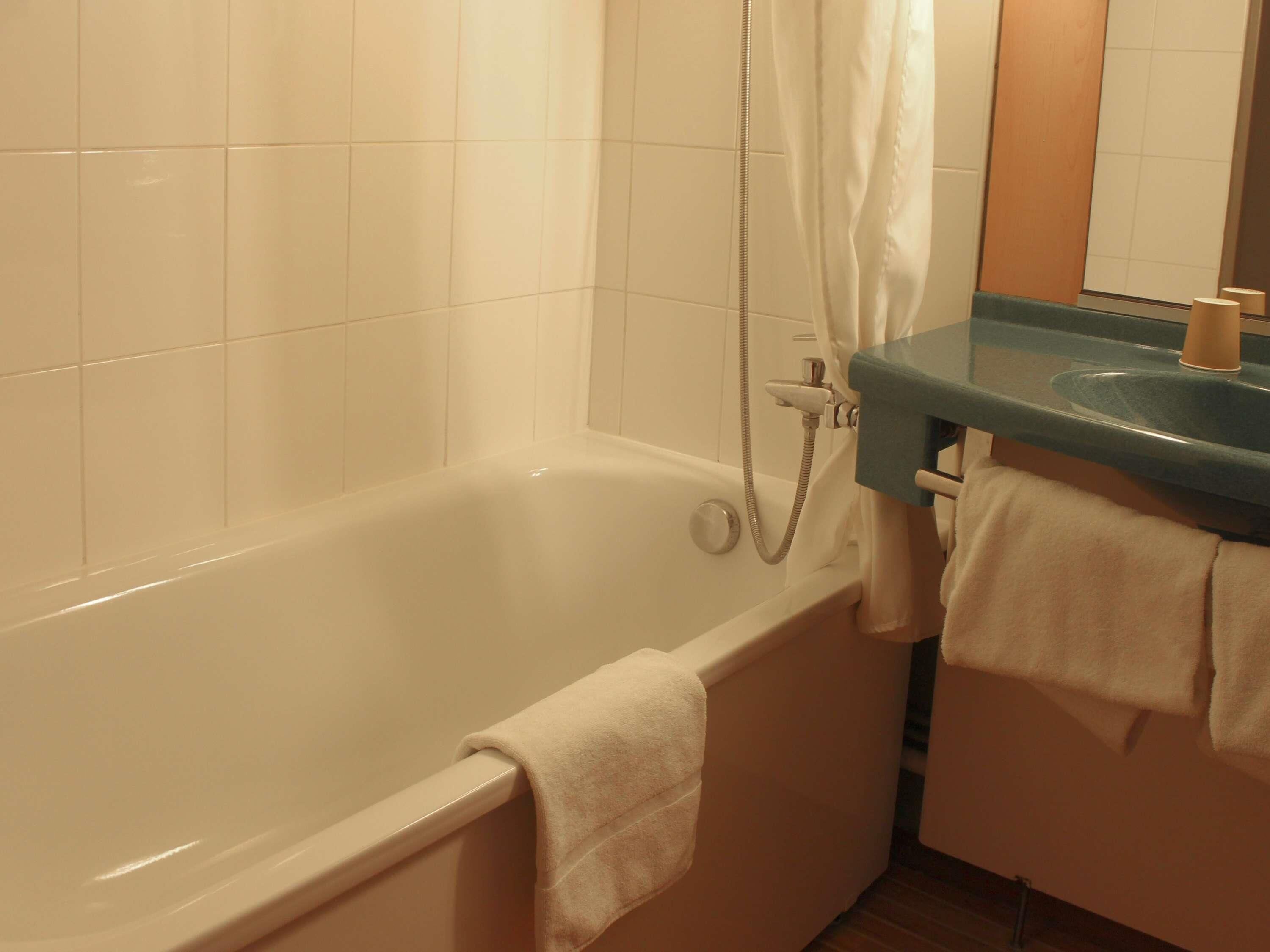 Een badkamer met een bad, een douche en een wastafel met een handdoekhouder.