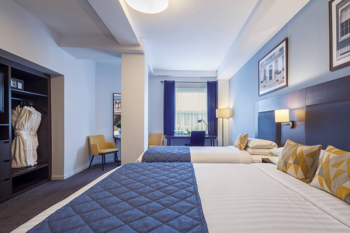 Hotellihuone, jossa on kaksi sänkyä, oleskelualue, vaatekaappi ja ikkuna, jossa on verhot.