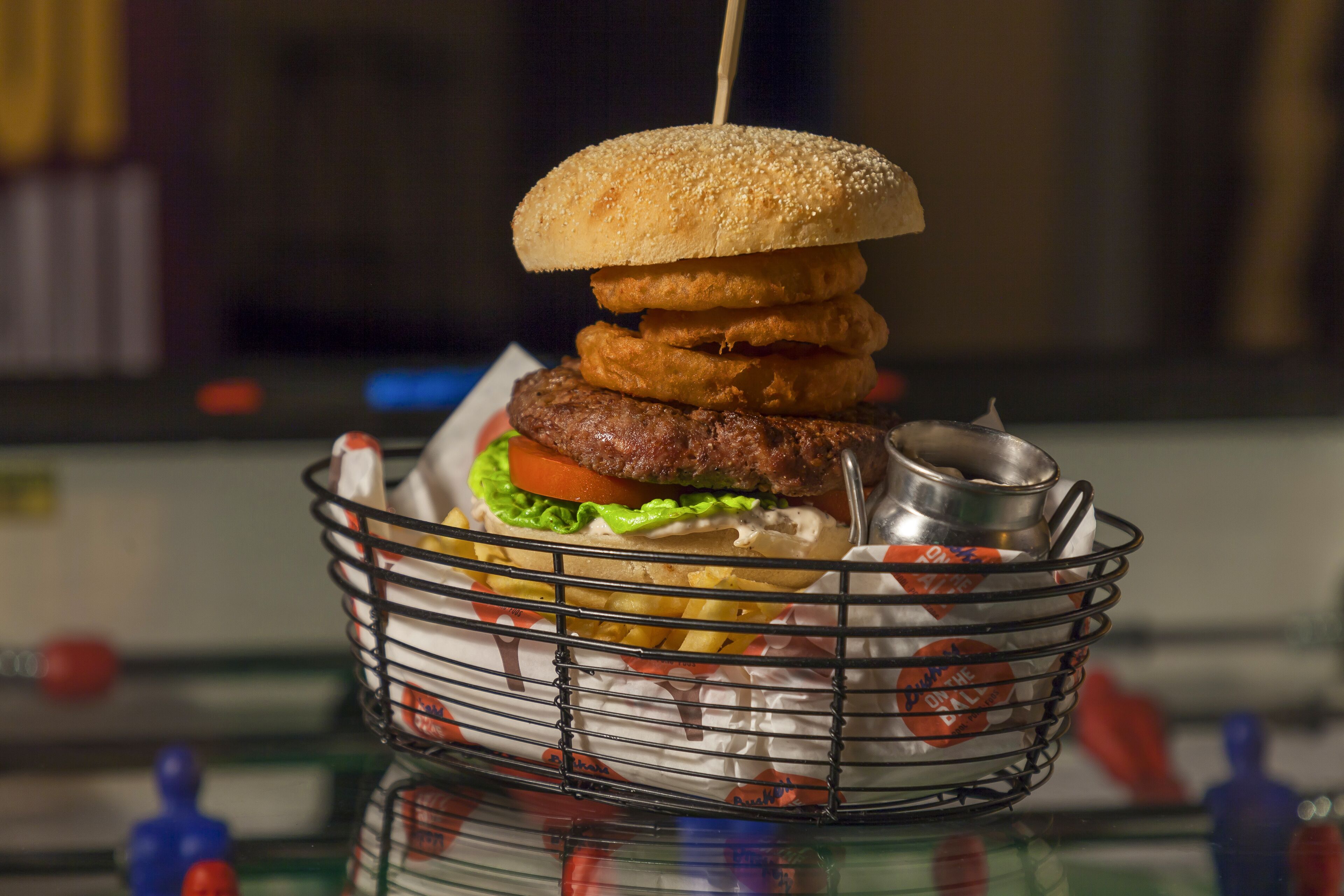 A burger with a sesame seed bun, lettuce, tomato, and a beef patty, served in a metal basket.
