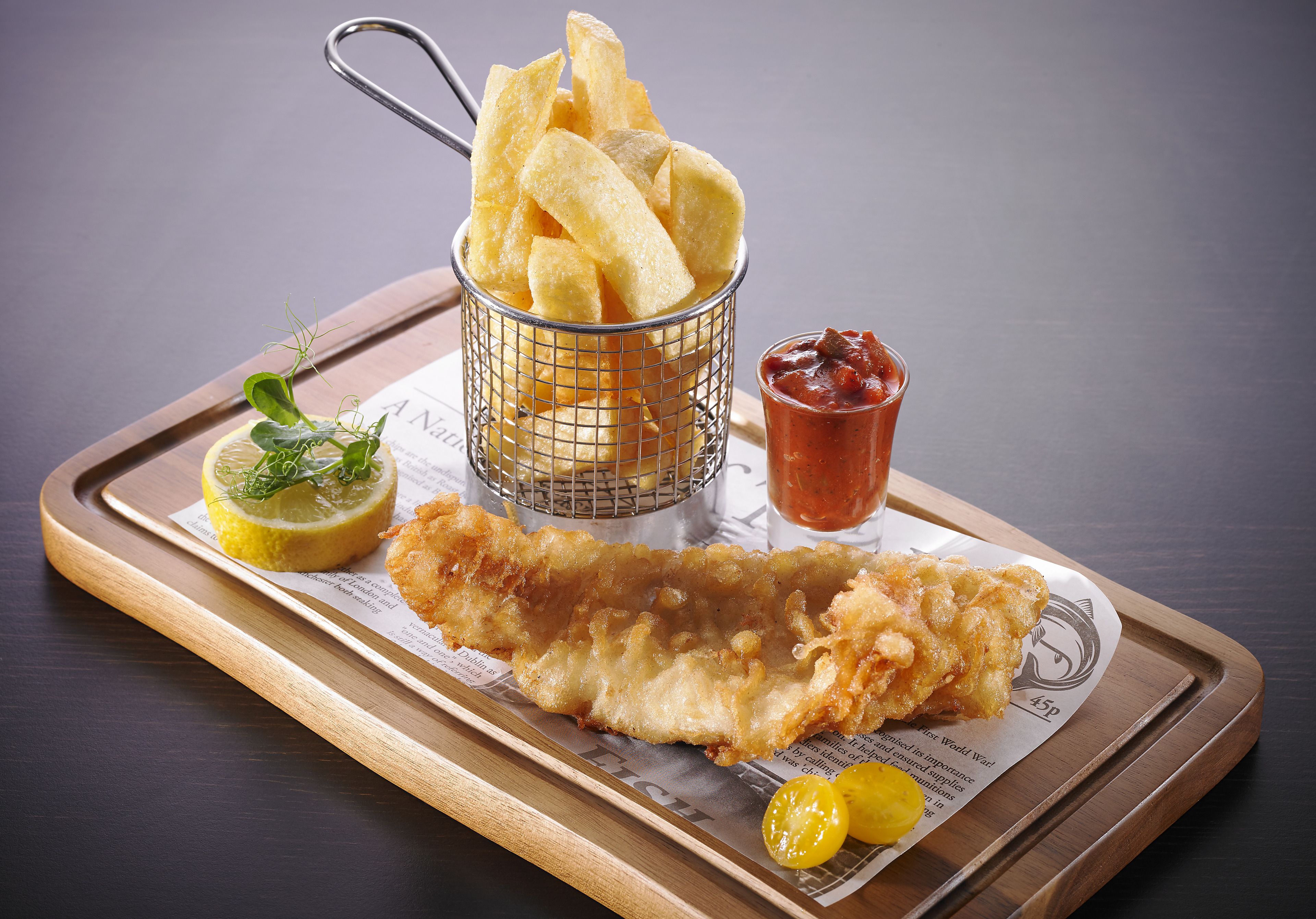 A tray with a fish and chips meal, lemon wedge, and ketchup.