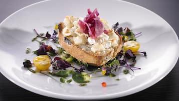 A white plate with a sandwich topped with cheese and garnished with red onion and greens, surrounded by a salad with various vegetables.