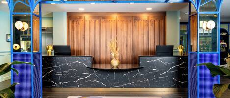 Un área de recepción con mostrador de mármol, panel de madera decorativo y puertas de vidrio con marco azul.
