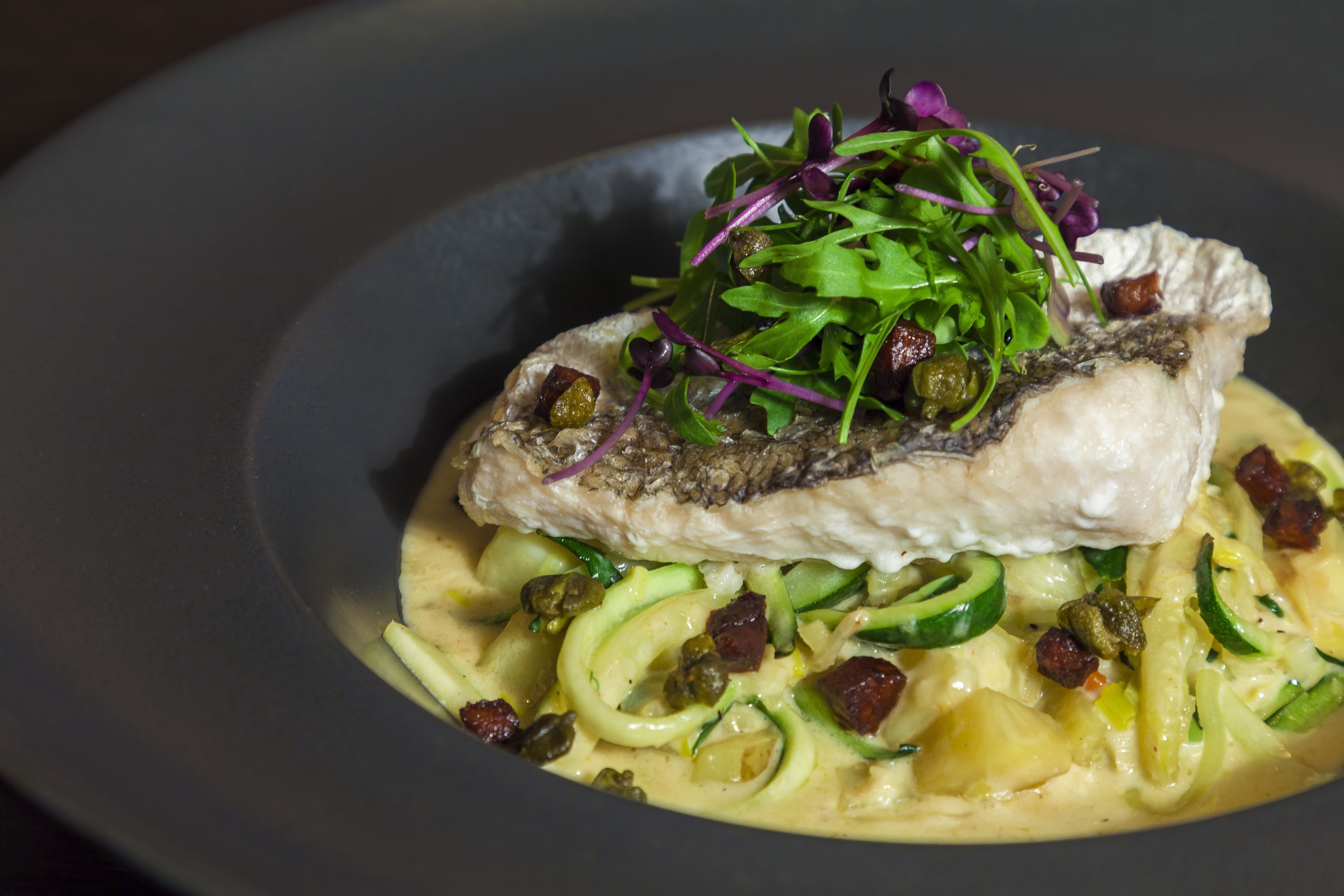 A dish with fish, greens, and pasta.