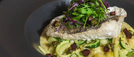A dish with fish, greens, and pasta.