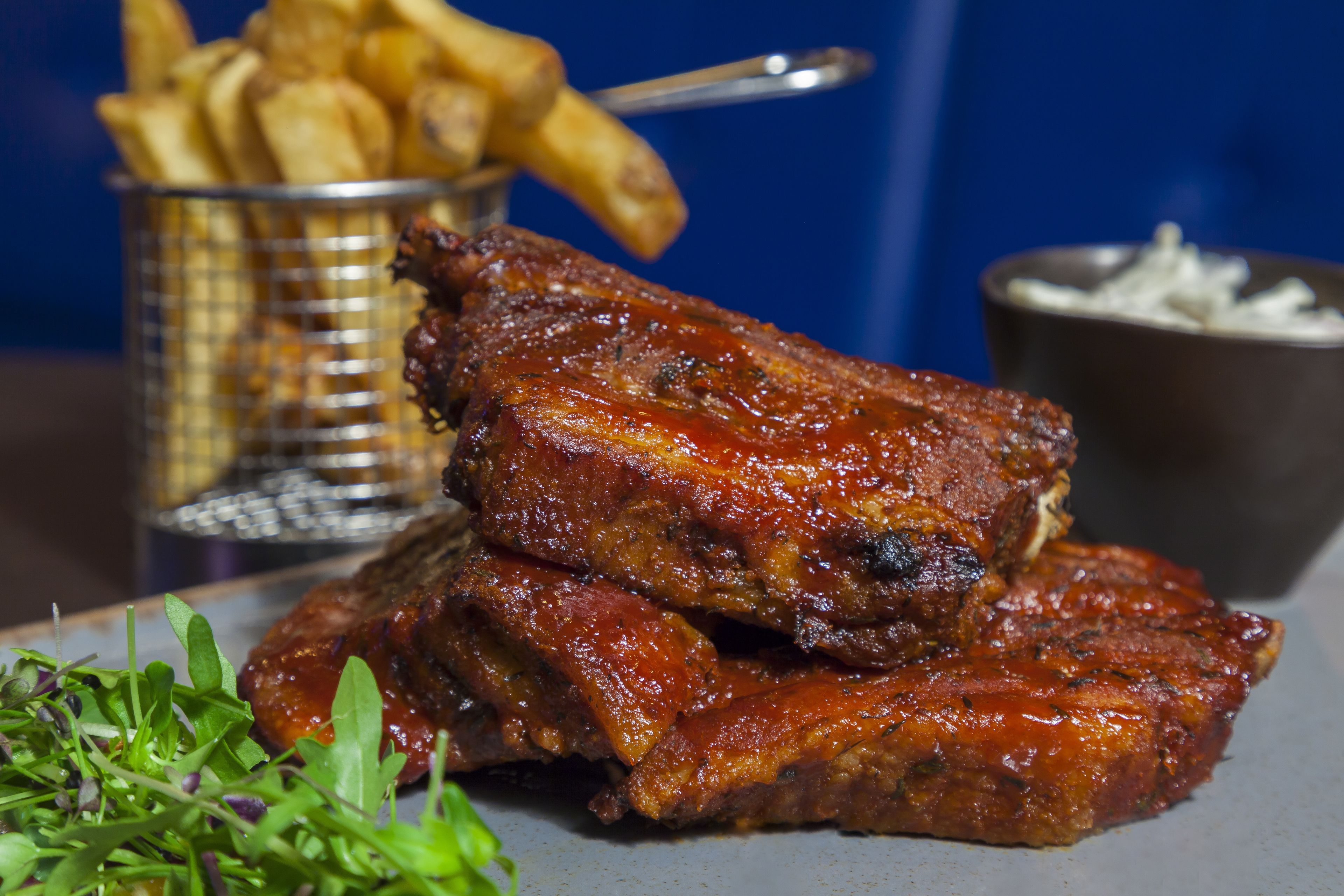 Ein Teller mit gegrillten Rippchen, Pommes und einer kleinen Sauce.