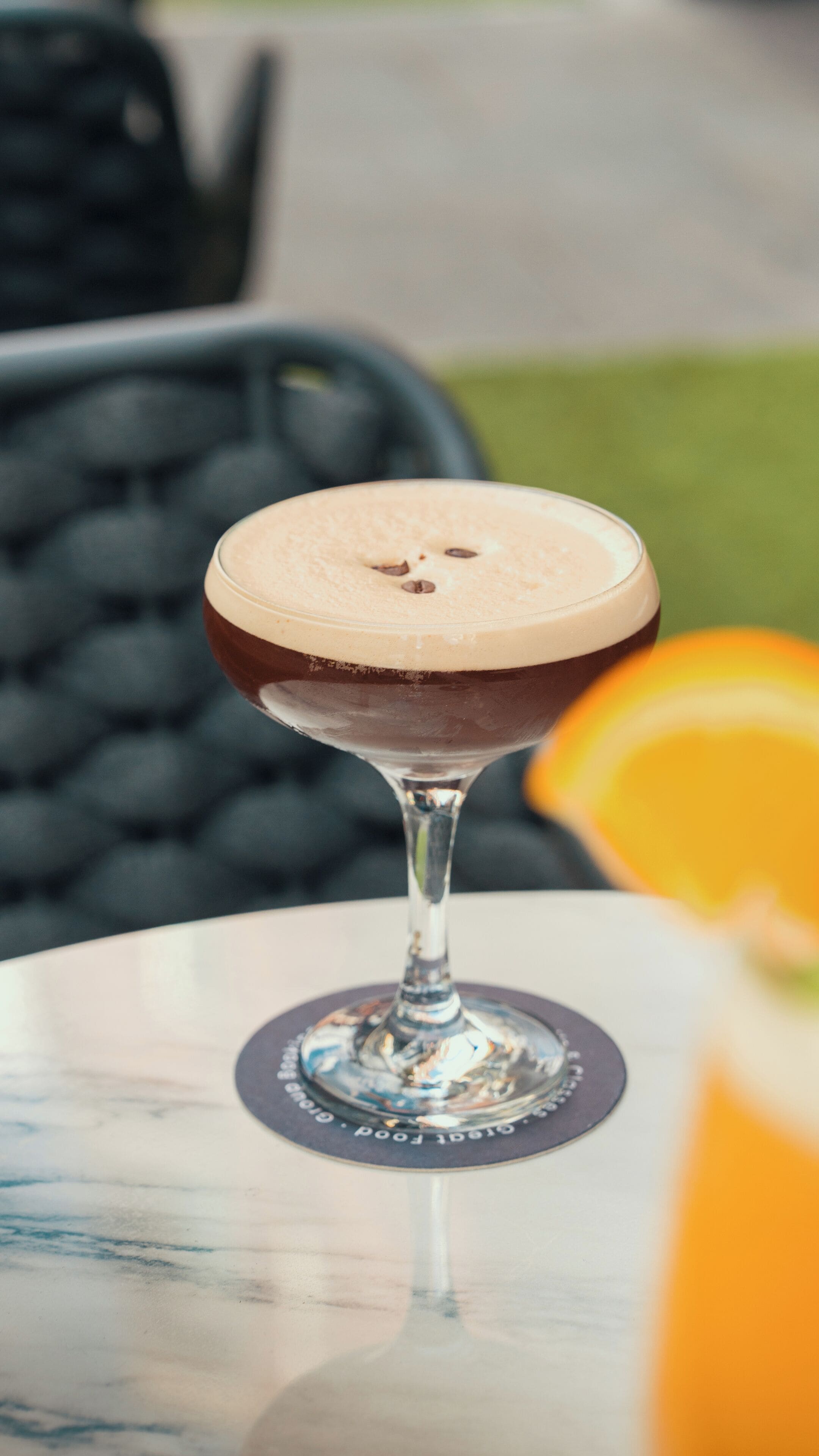 A cocktail in a martini glass on a table with a coaster.