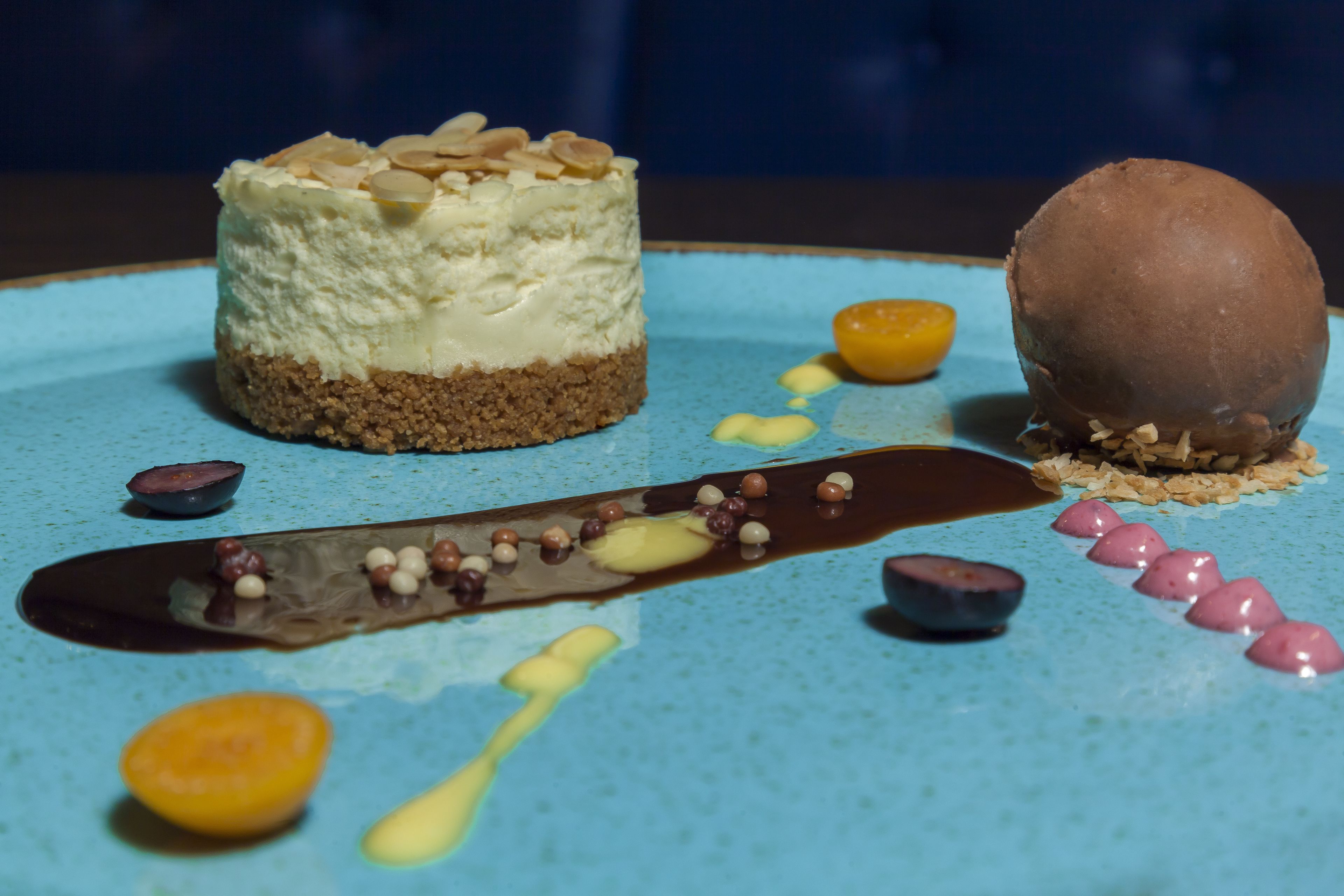 Un piattino da dessert con una torta a strati, una sfera di cioccolato e diversi elementi decorativi.