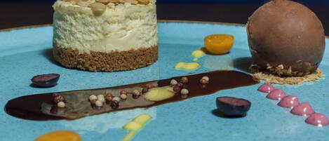 Un piattino da dessert con una torta a strati, una sfera di cioccolato e diversi elementi decorativi.