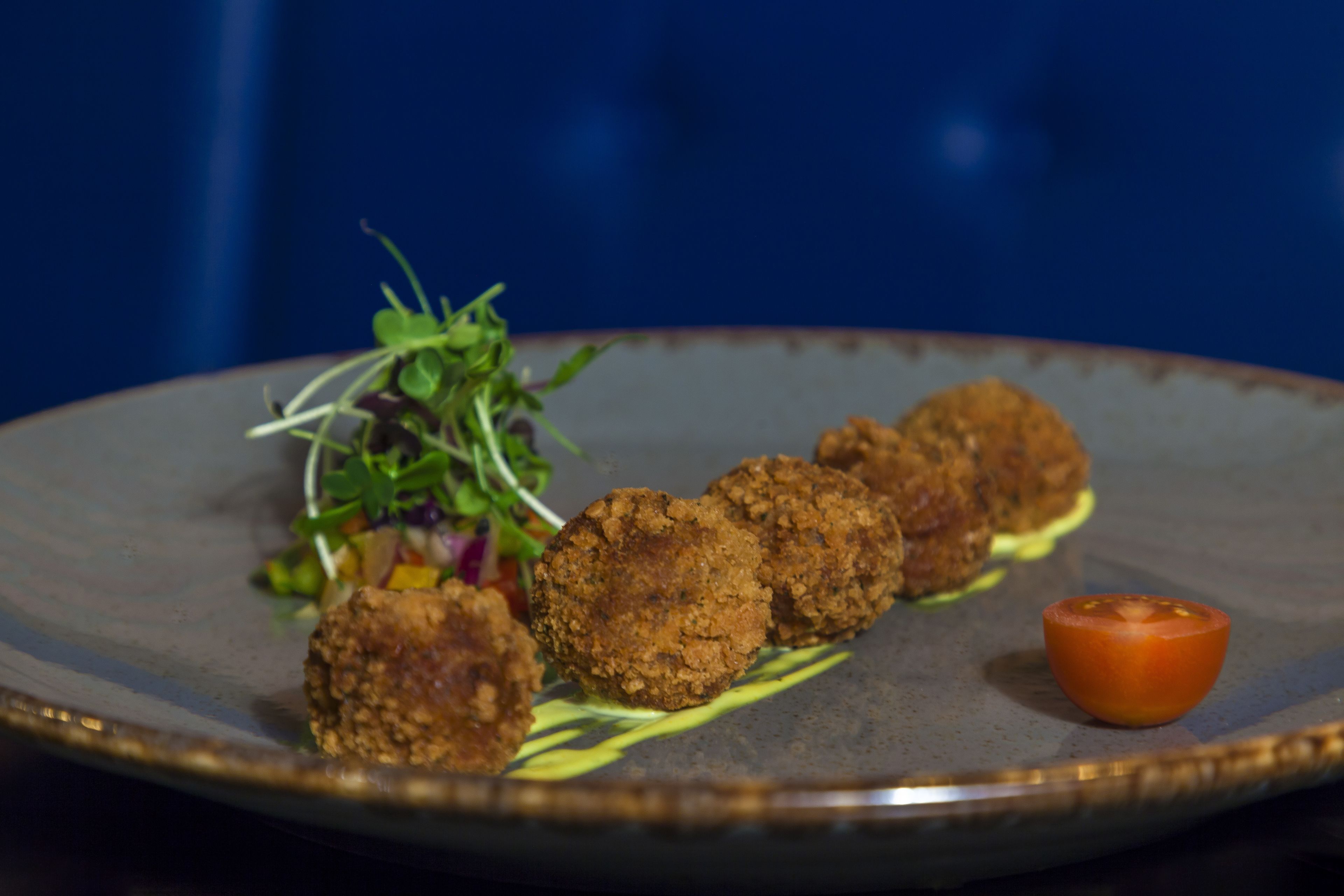 A plate with three fried patties, a small tomato, and a salad.