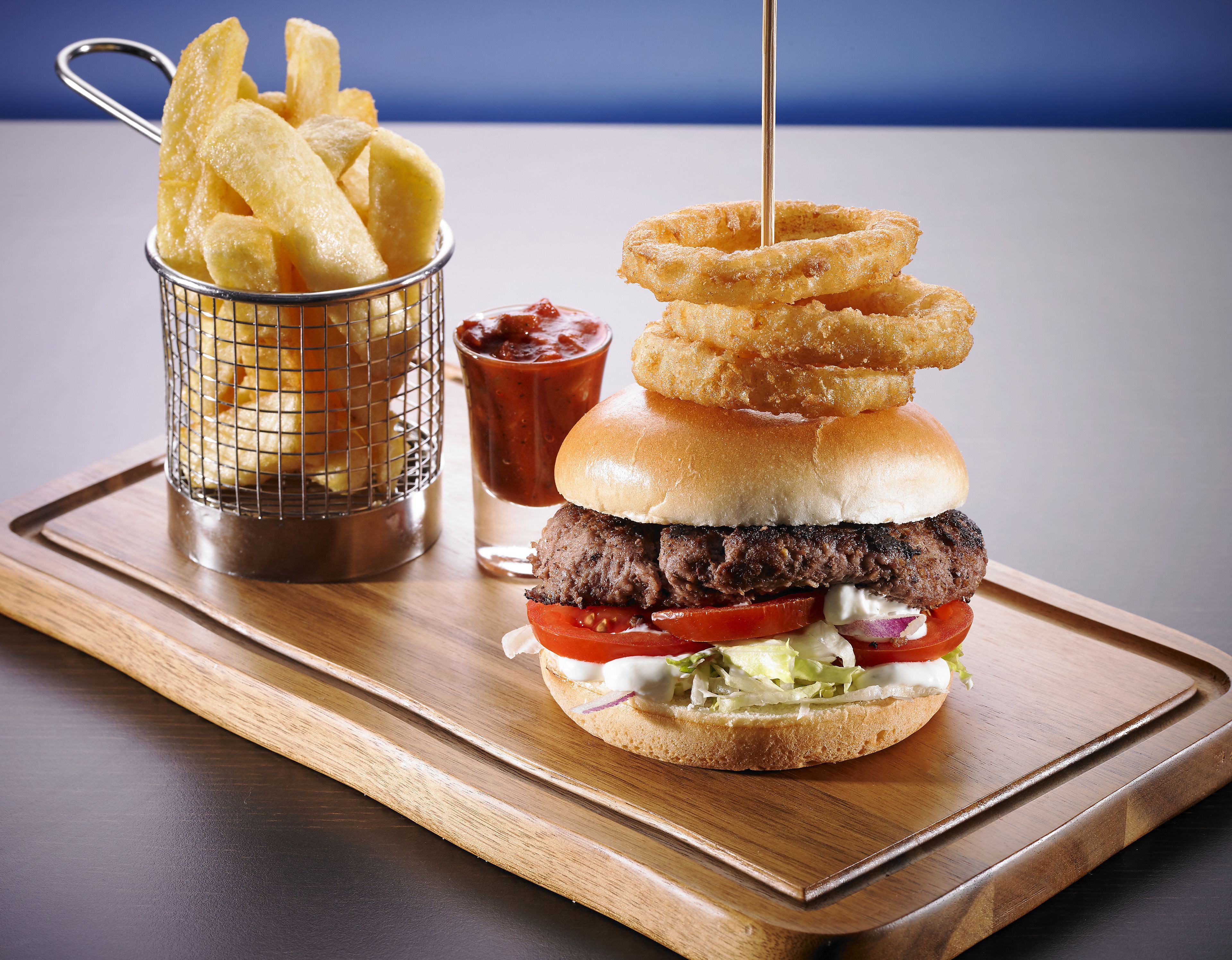 Hamburguesa con carne, lechuga, tomate y cebolla, servida en un pan con aros de cebolla y kétchup.