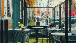An outdoor cafe with round tables and chairs, a glass display case, and a view of the street.