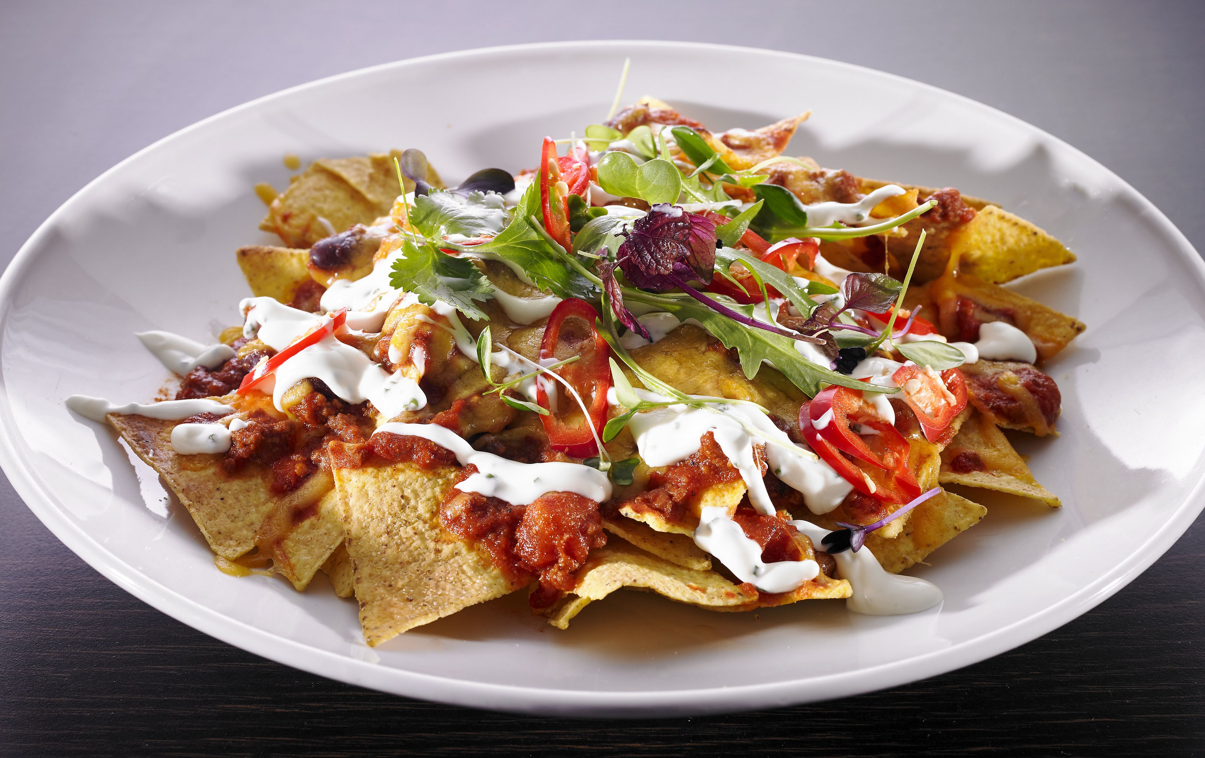 Ein Teller Nachos mit Käse, Tomaten und Salat.