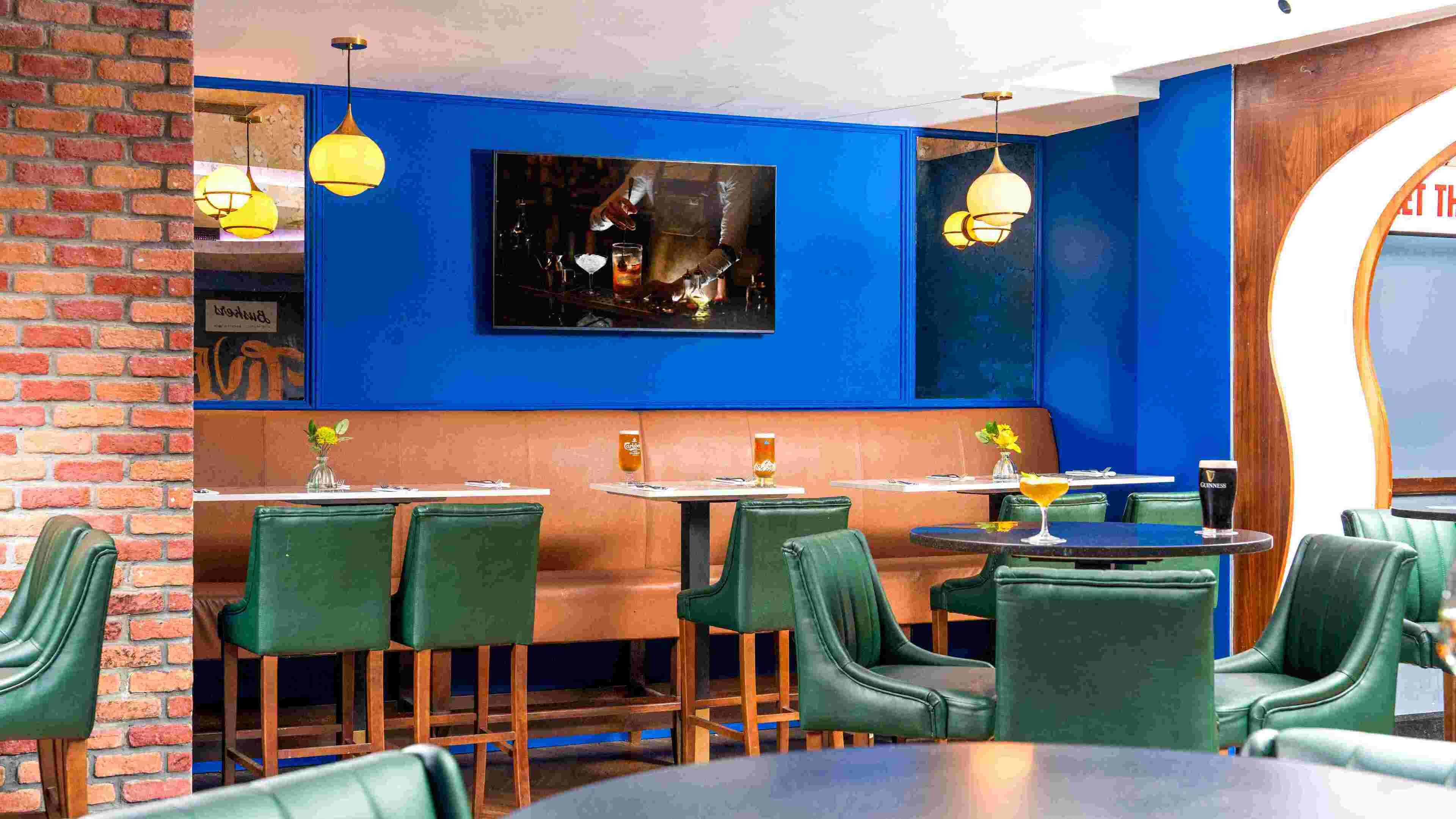 A restaurant interior with brick walls, green upholstered chairs, and blue walls.