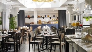 A spacious dining area with multiple tables and chairs, a central counter with food displays, and a modern chandelier.
