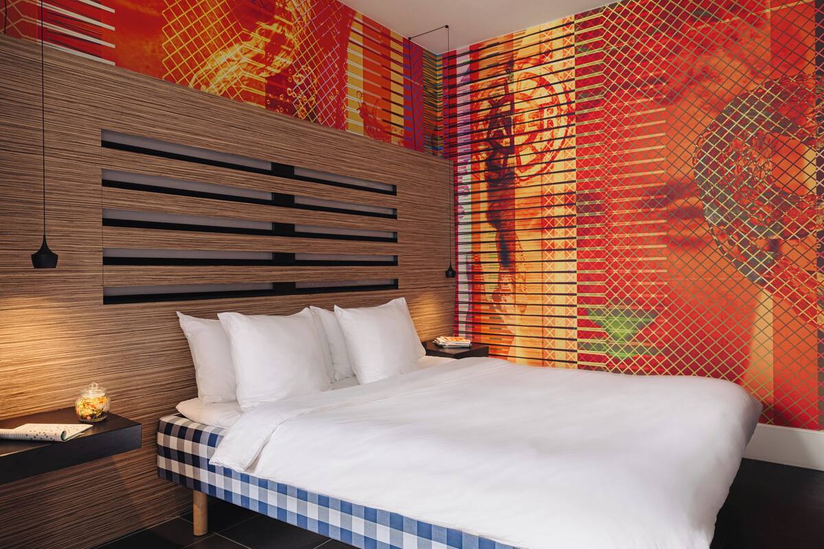 A modern bedroom with a wooden headboard, a checkered bedspread, and a vibrant abstract wall mural.
