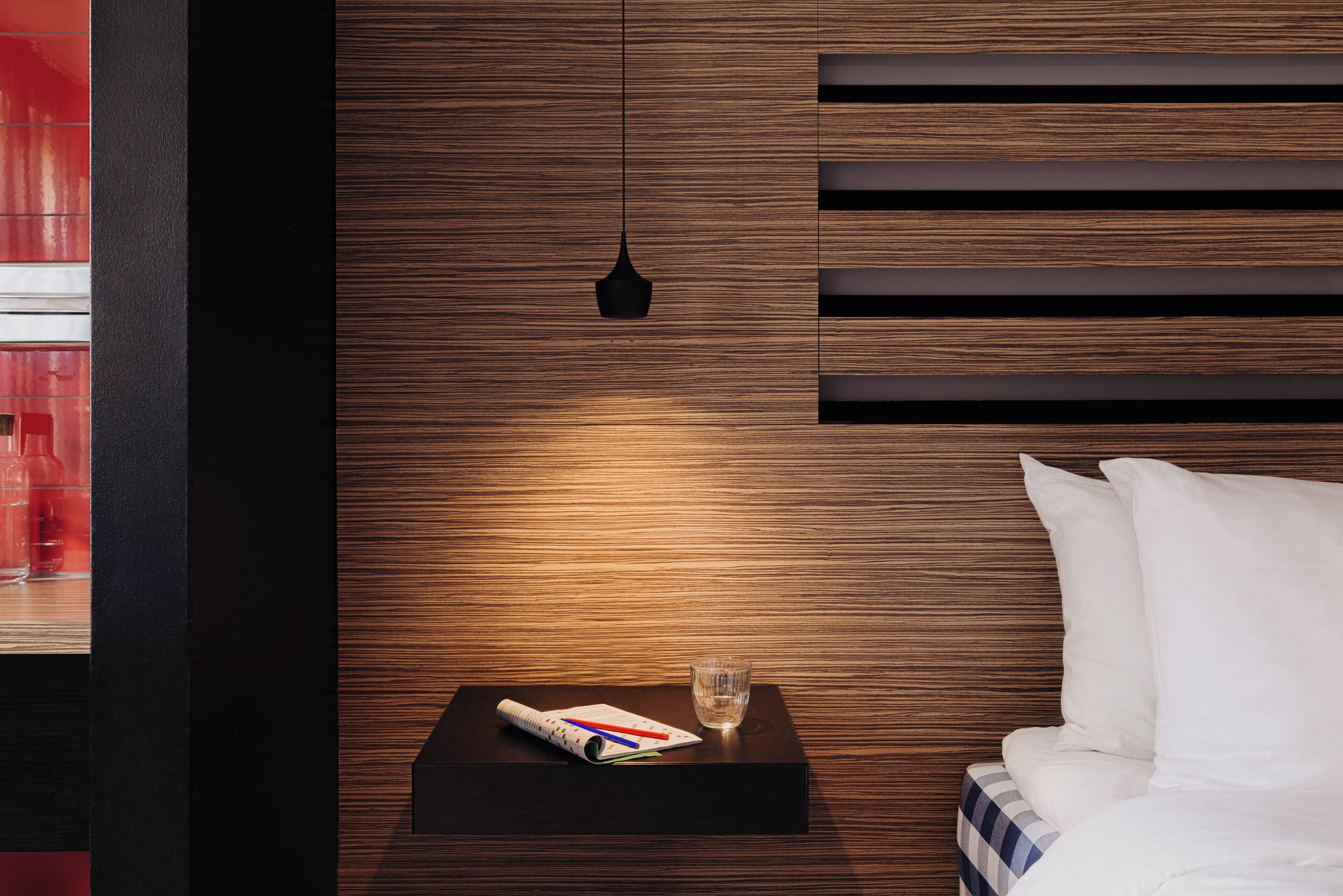 A neatly made bed with white linens, a bedside table with a glass of water, a notebook, and pens.