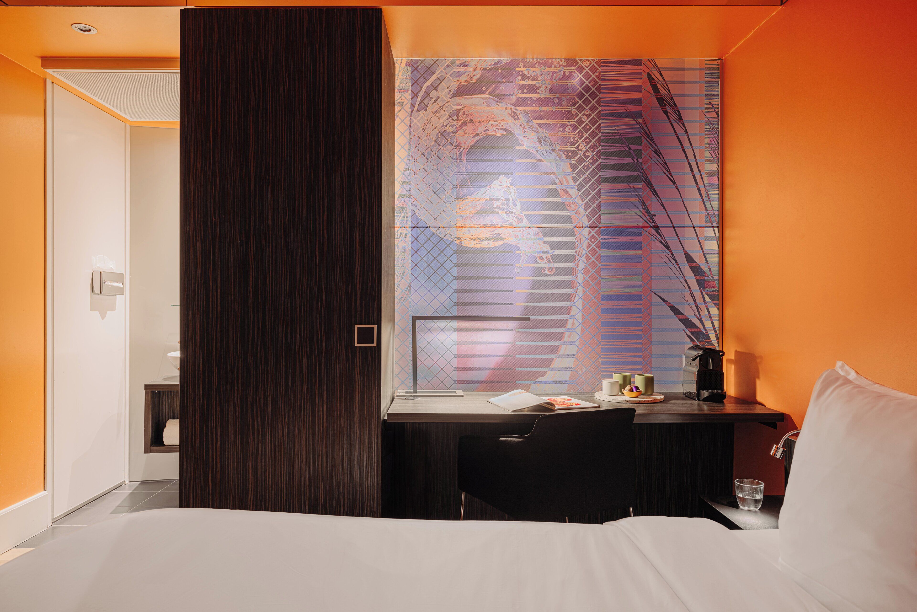 Una camera d'albergo moderna con un letto grande, una scrivania con un computer e un'ampia finestra con motivo geometrico.