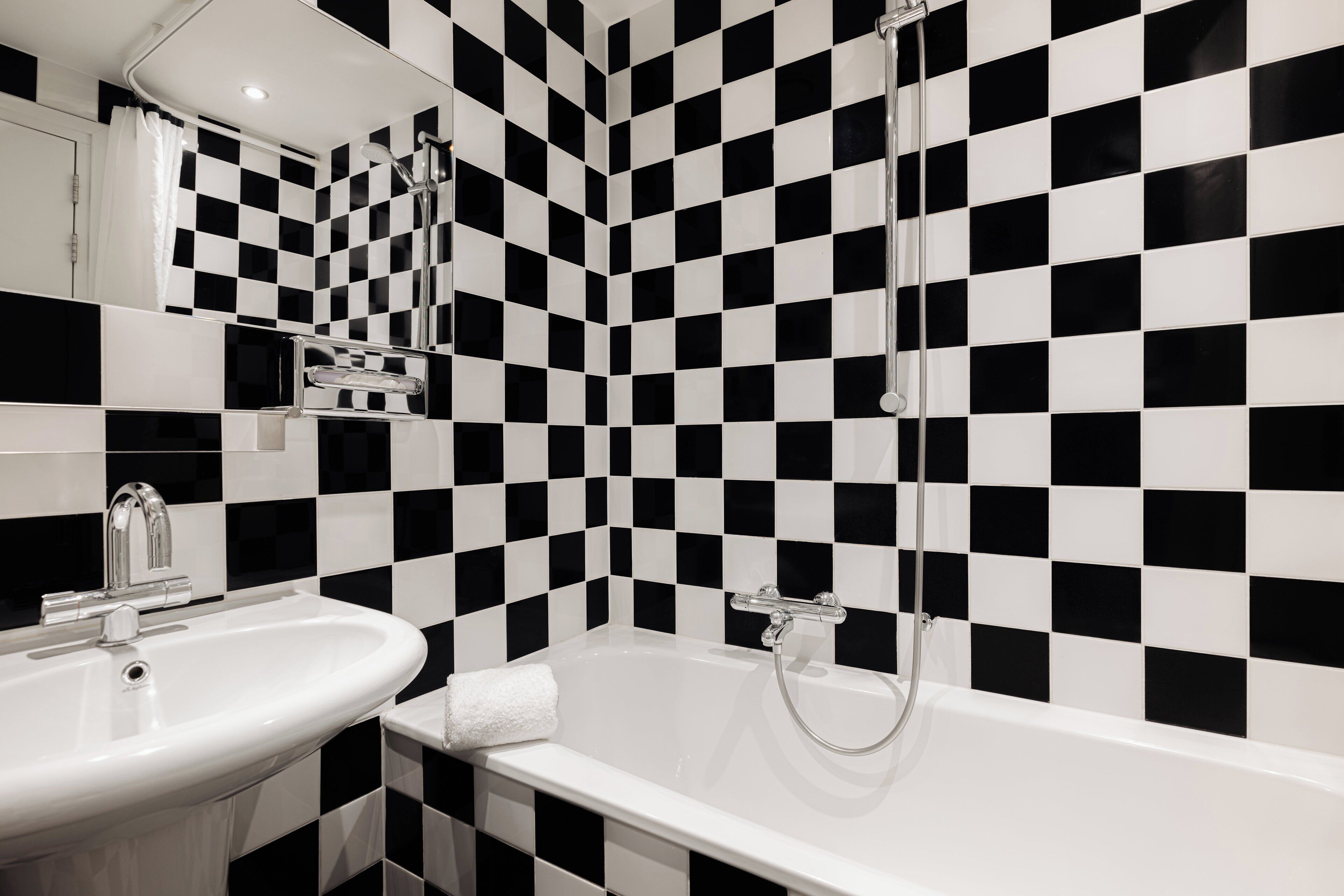 A bathroom with a checkered black and white tile wall, a white sink, and a bathtub with a showerhead.