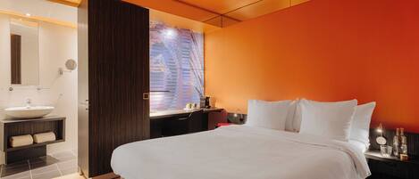 Un hotel moderno con una cama grande, un baño con lavamanos y espejo, y vistas a un edificio a través de una ventana.