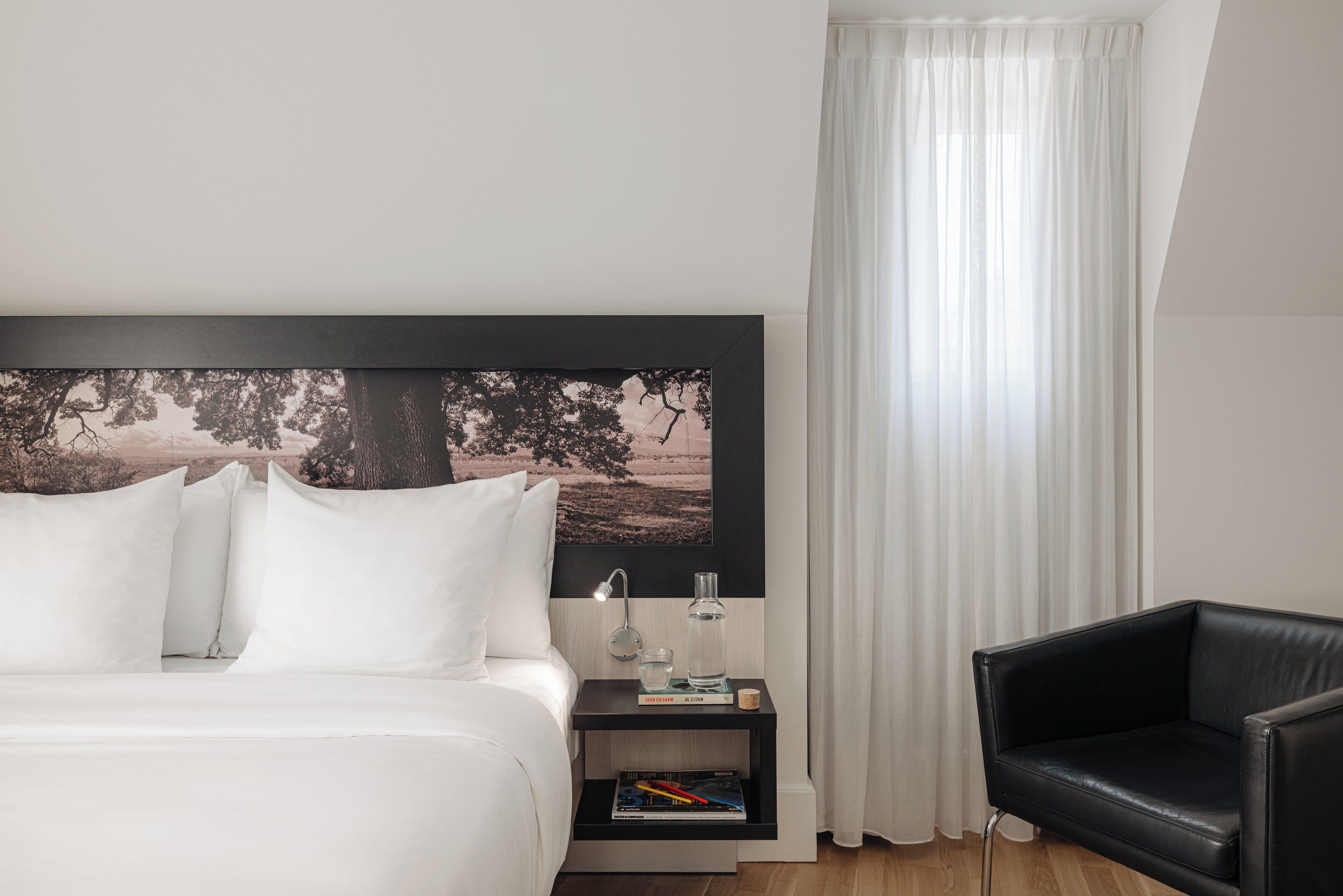 Camera d'albergo ordinata con un letto grande, un tavolino con una lampada, una poltrona in pelle nera e un quadro appeso al muro.