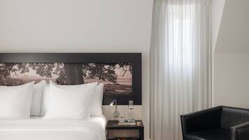 Camera d'albergo ordinata con un letto grande, un tavolino con una lampada, una poltrona in pelle nera e un quadro appeso al muro.